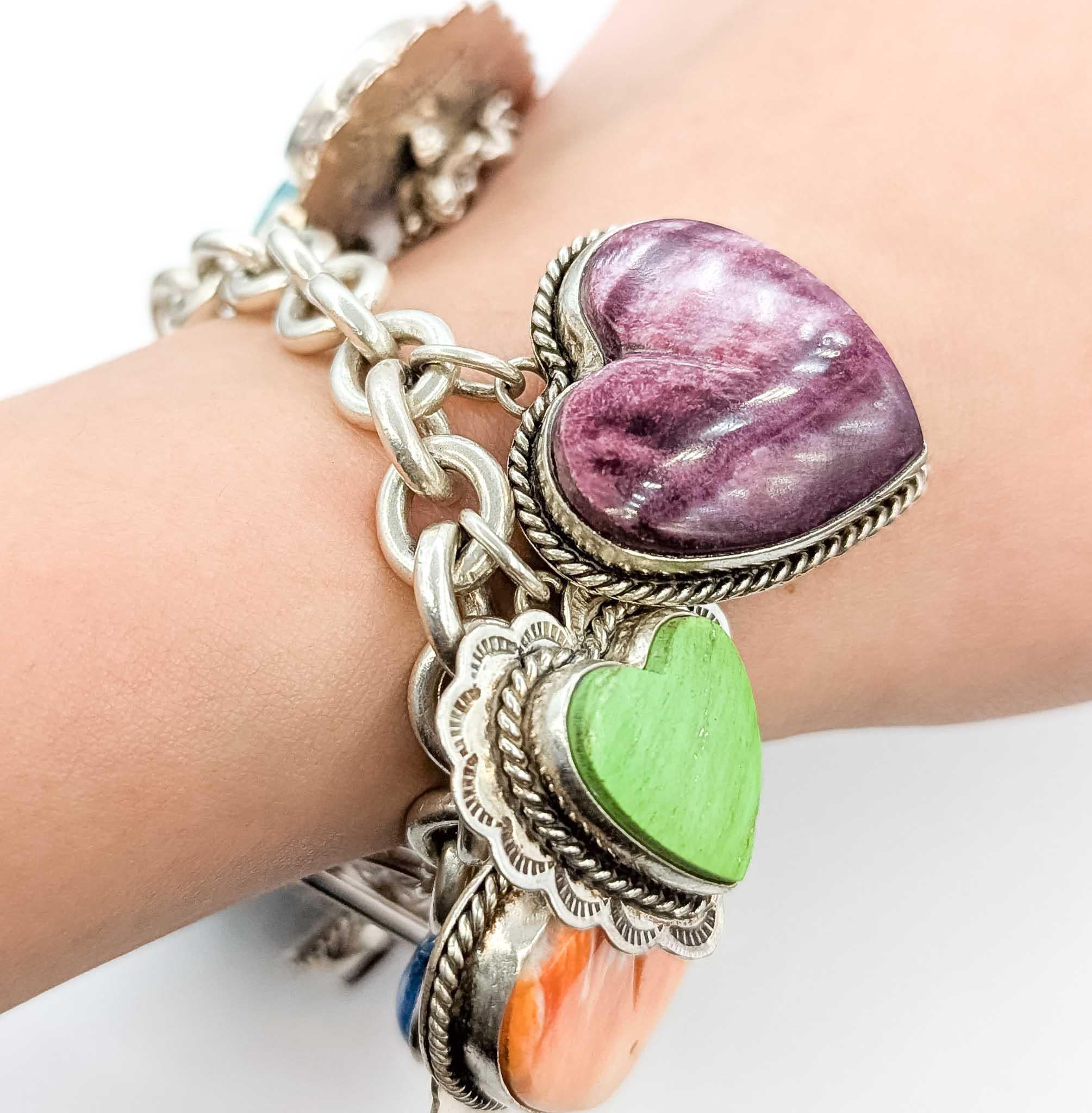 This bold and collectible bracelet by designer Joan Slifka is crafted in solid sterling silver and adorned with an array of vibrant gemstone heart charms. Measuring 7.5 inches in length and weighing over 120 grams, this substantial bracelet features