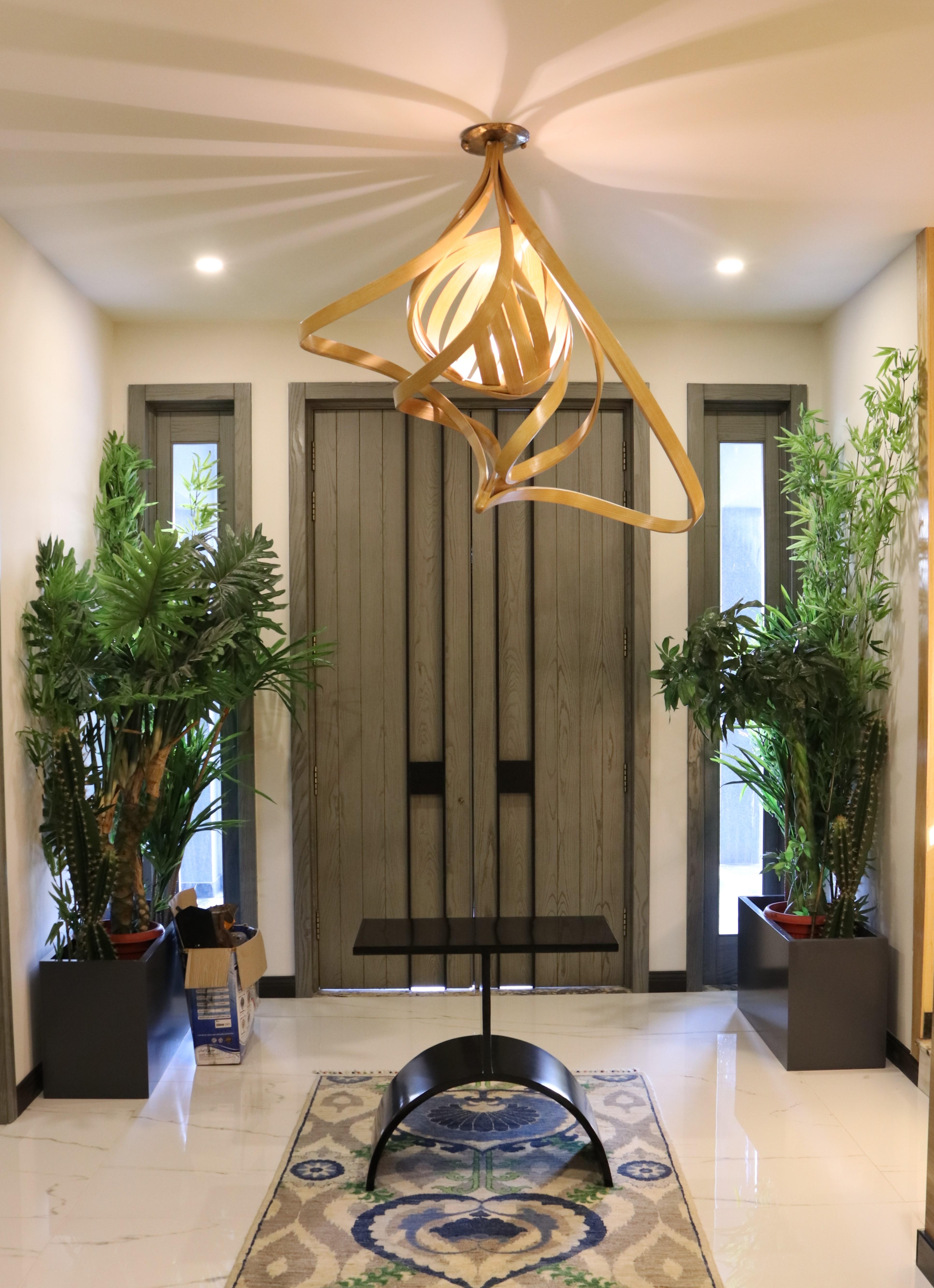 A chandelier made in solid ashwood using wood bending techniques. A single light is placed in a wooden cocoon which releases light with linear gaps creating a distinct lighting ambiance. This is further layered with bentwood designs surrounding the