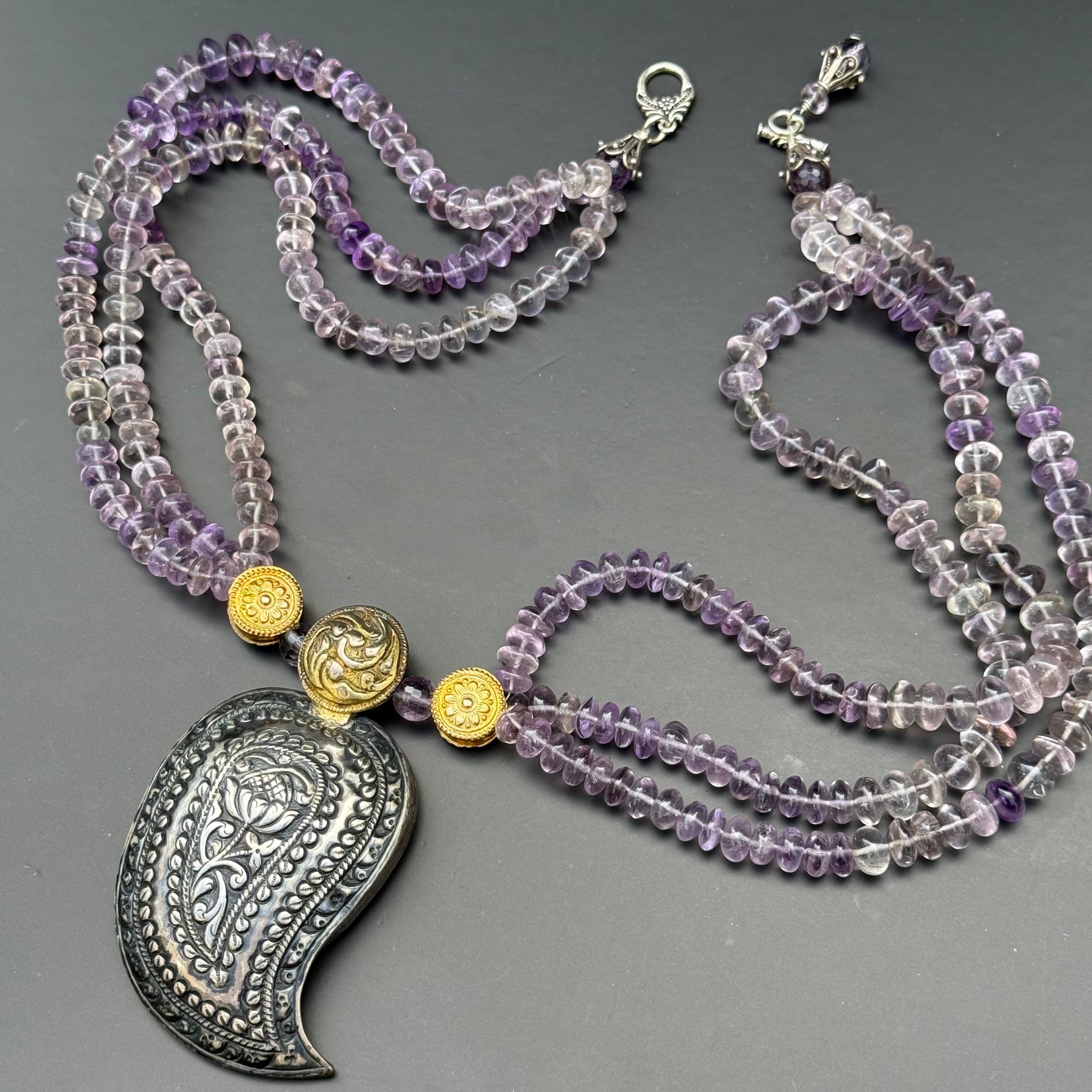 Ce collier unique s'articule autour d'une boucle rare en argent ancien, façonnée de manière complexe dans une forme stylisée de mangue ou de cachemire - un motif emblématique aux racines symboliques profondes dans les arts décoratifs de l'Asie du