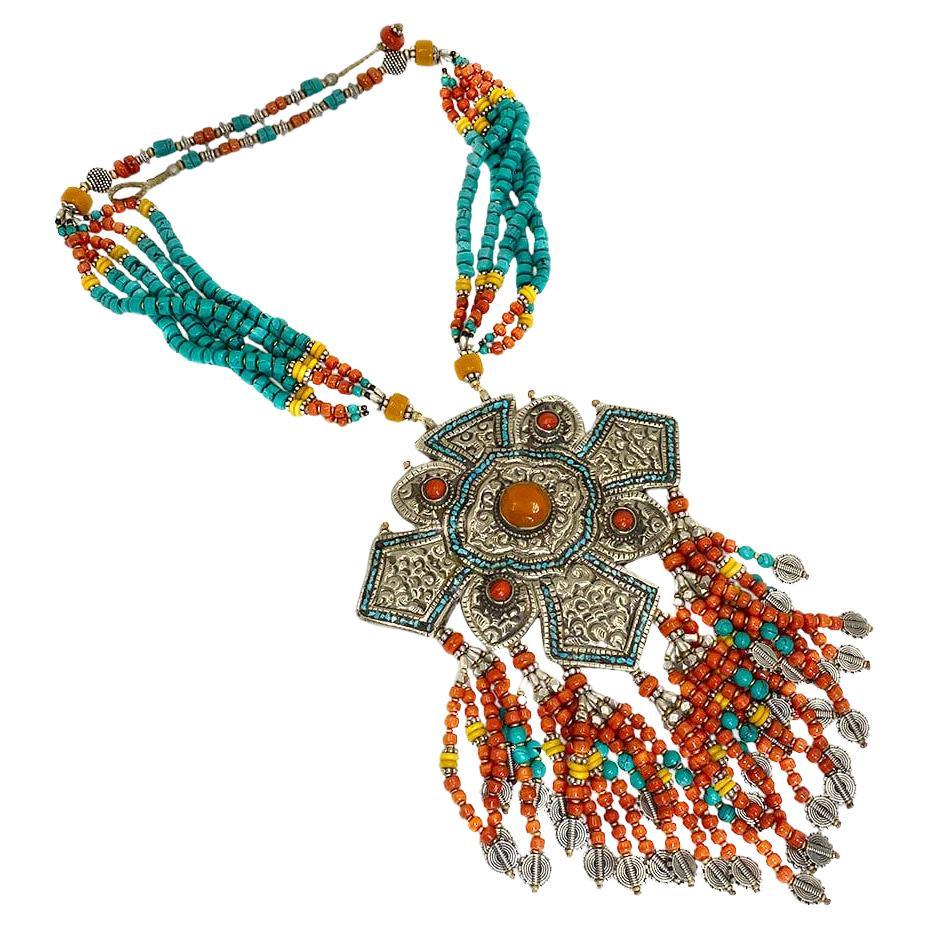Si tratta di una collana con placca in Nepal e frange. Questa collana di perline in seta colorata in stile etnico è incentrata su una placca in argento del Nepal con motivo tradizionale di 3,5 x 4,5 pollici e intarsi in turchese, corallo incastonato