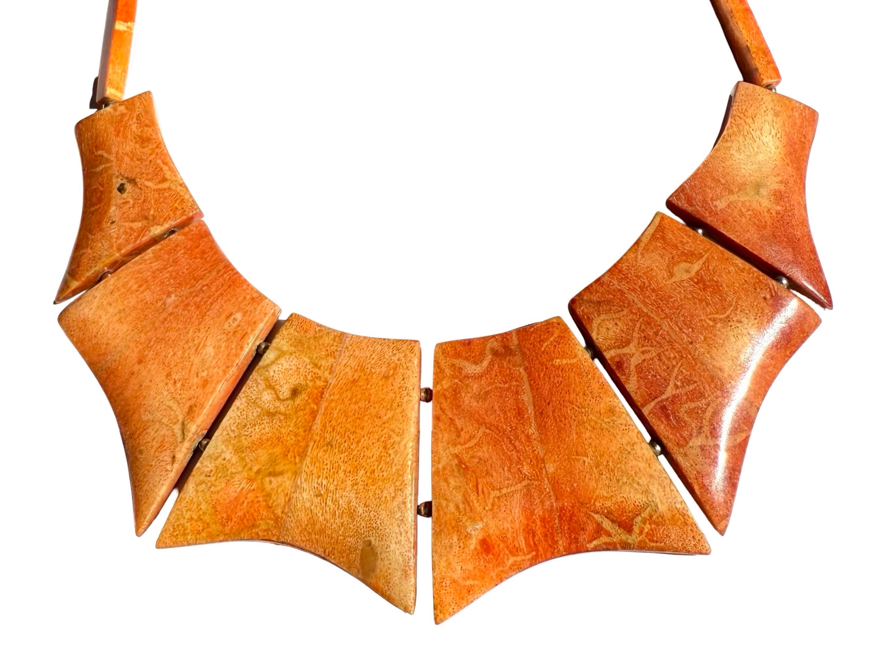 Die Kette besteht aus mehreren Stücken Apfelkoralle, jedes mit einer eigenen Form und natürlichen Mustern, die zu einem latzähnlichen Design verbunden sind. Die Segmente variieren in Größe und Kontur, was die organische und handwerkliche Ästhetik