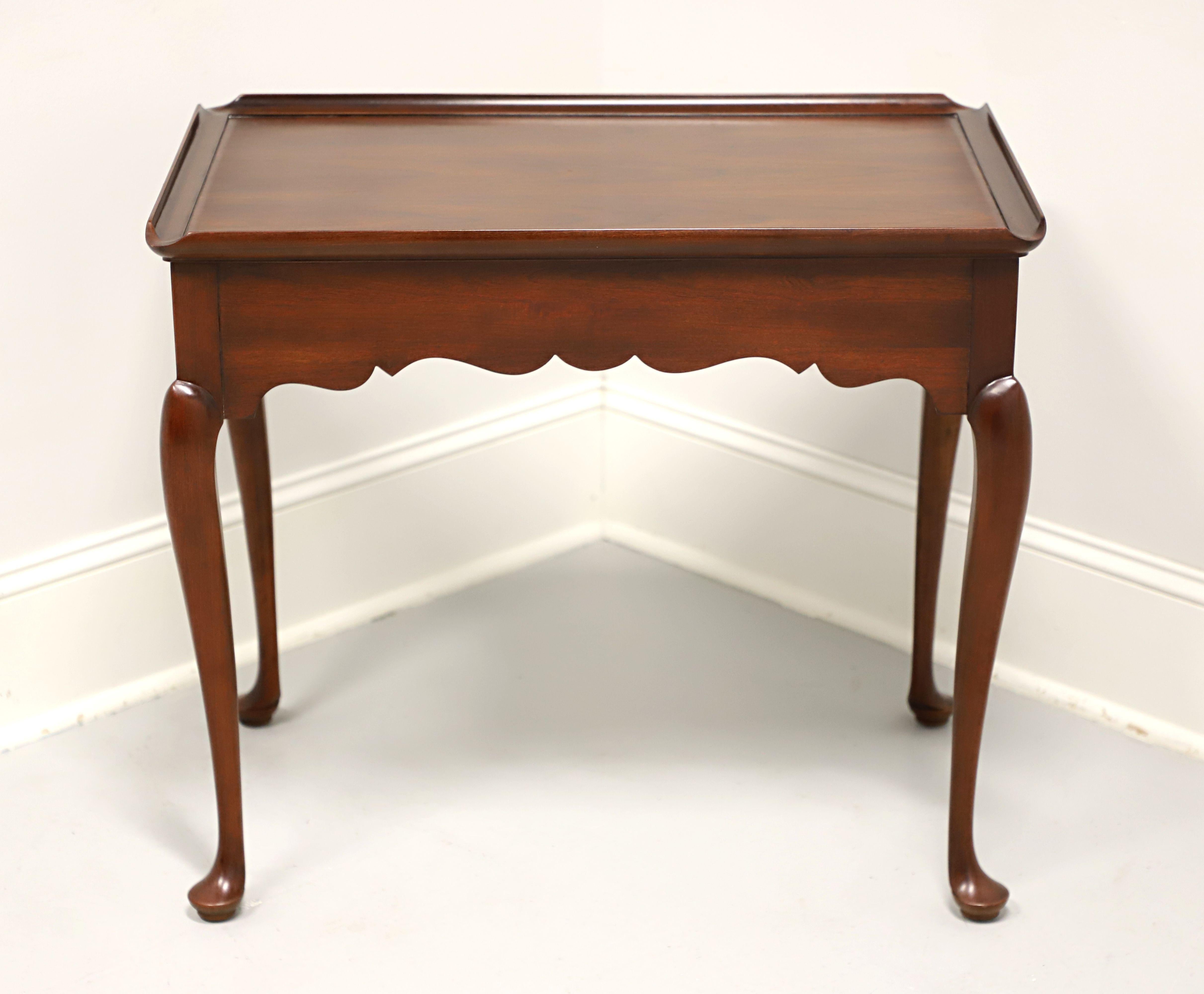 A tea table in the Queen Anne style by Statton Furniture. Solid cherry wood with their Centennial finish, two side slide out trays with brass knobs, carved apron, tapered legs and pad feet. Made in Hagerstown, Maryland, USA, in the late 20th