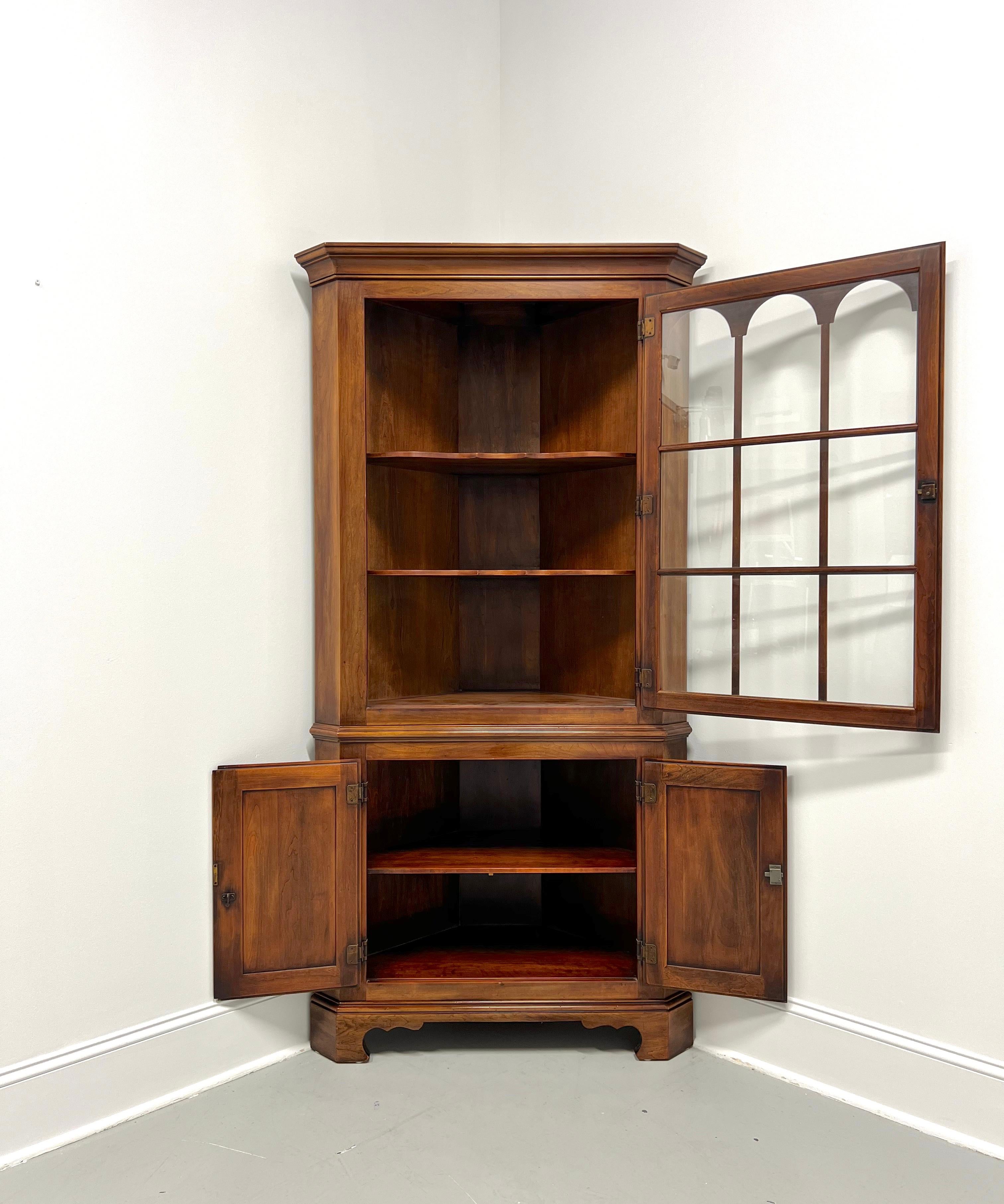 A Chippendale style corner cupboard by Statton Furniture. Solid cherry wood with their Oxford Antique finish, brass hardware, crown molding to top, an ogee edge dividing the sections, and carved bracket feet. Upper cabinet features two fixed
