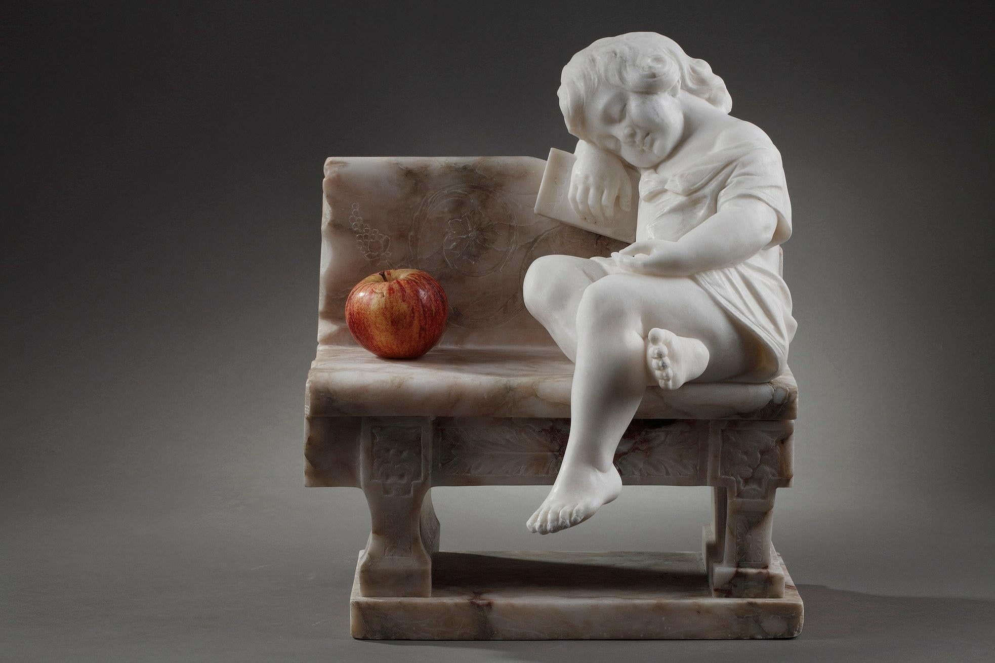 This sculpture is made of alabaster and marble. A young child, in alabaster, dressed in a short open shirt, is asleep with his legs crossed. His hair form a curl around his left ear. He is using a book with the first four letters of the alphabet as