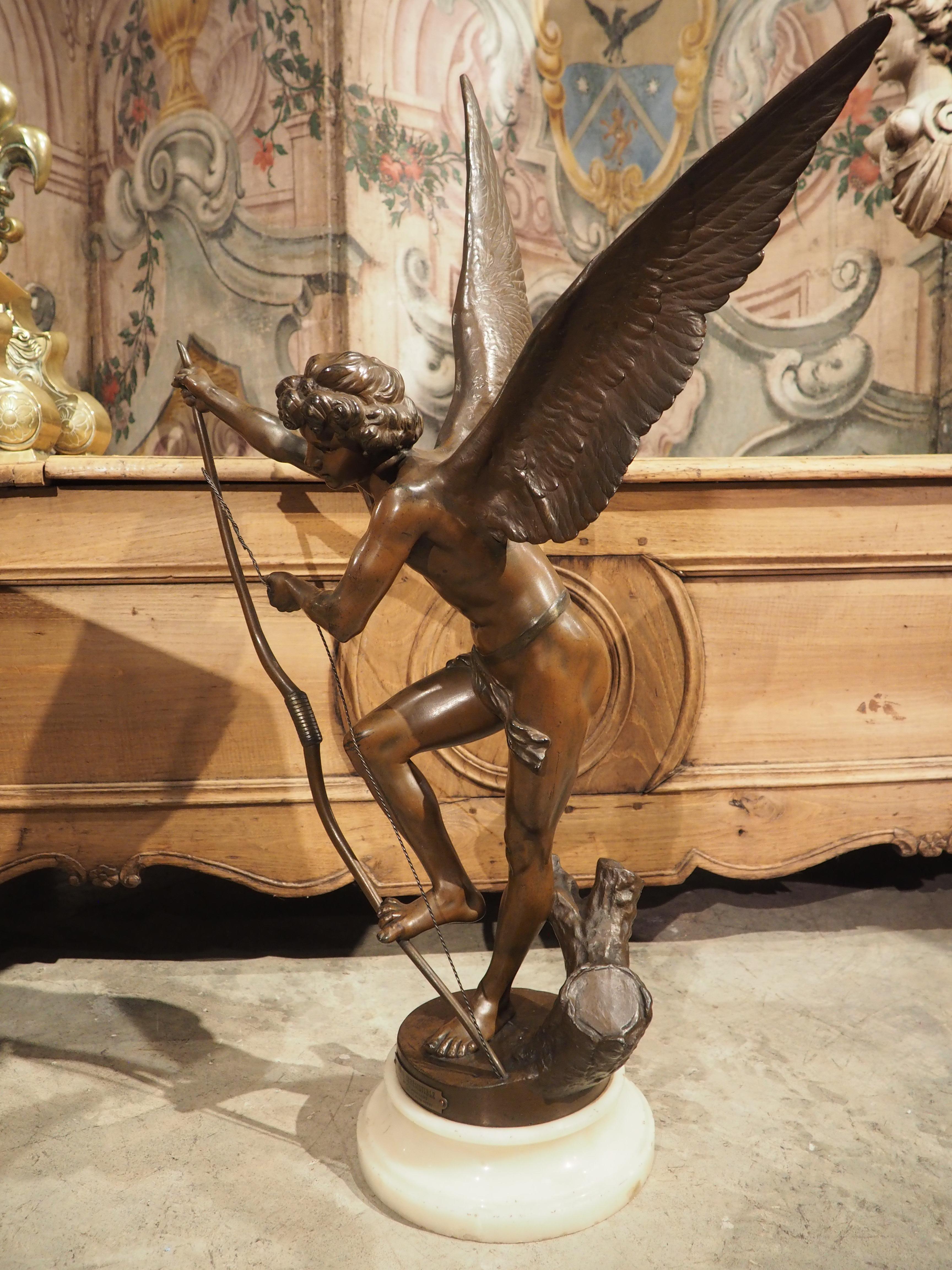 After the original sculpture by Maria Cassavetti, this metal statue on an alabaster base depicts Cupid stringing his bow. A small stump can be seen behind Cupid’s left foot, as he uses his right foot and right hand to bend the bow while he holds the