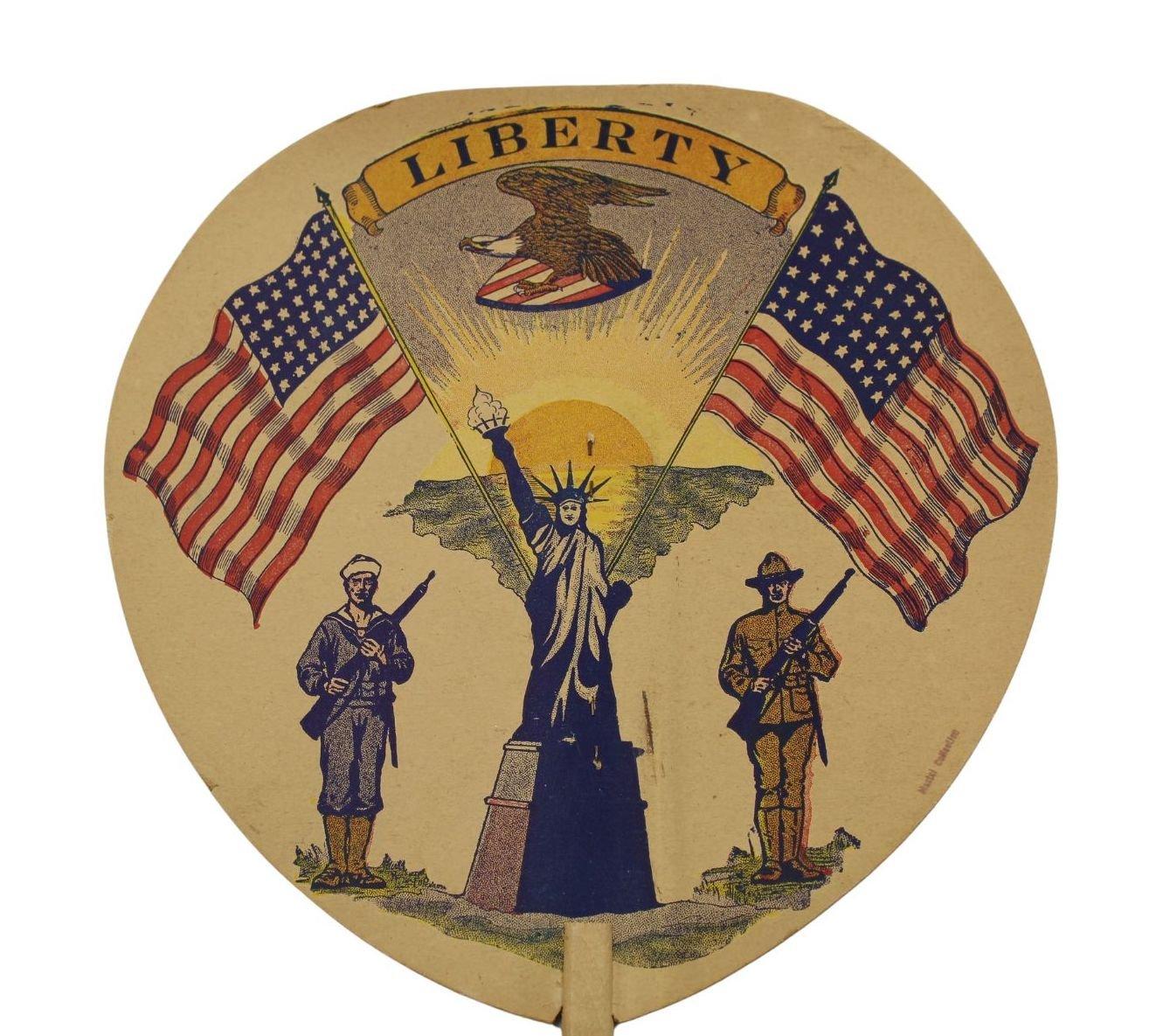 Presented is a Statue of Liberty patriotic printed paddle fan from the early 20th century. At center, the Statue of Liberty stands tall, her shining torch held above her head. On either side of the statue are large, waving 48-star American flags. At
