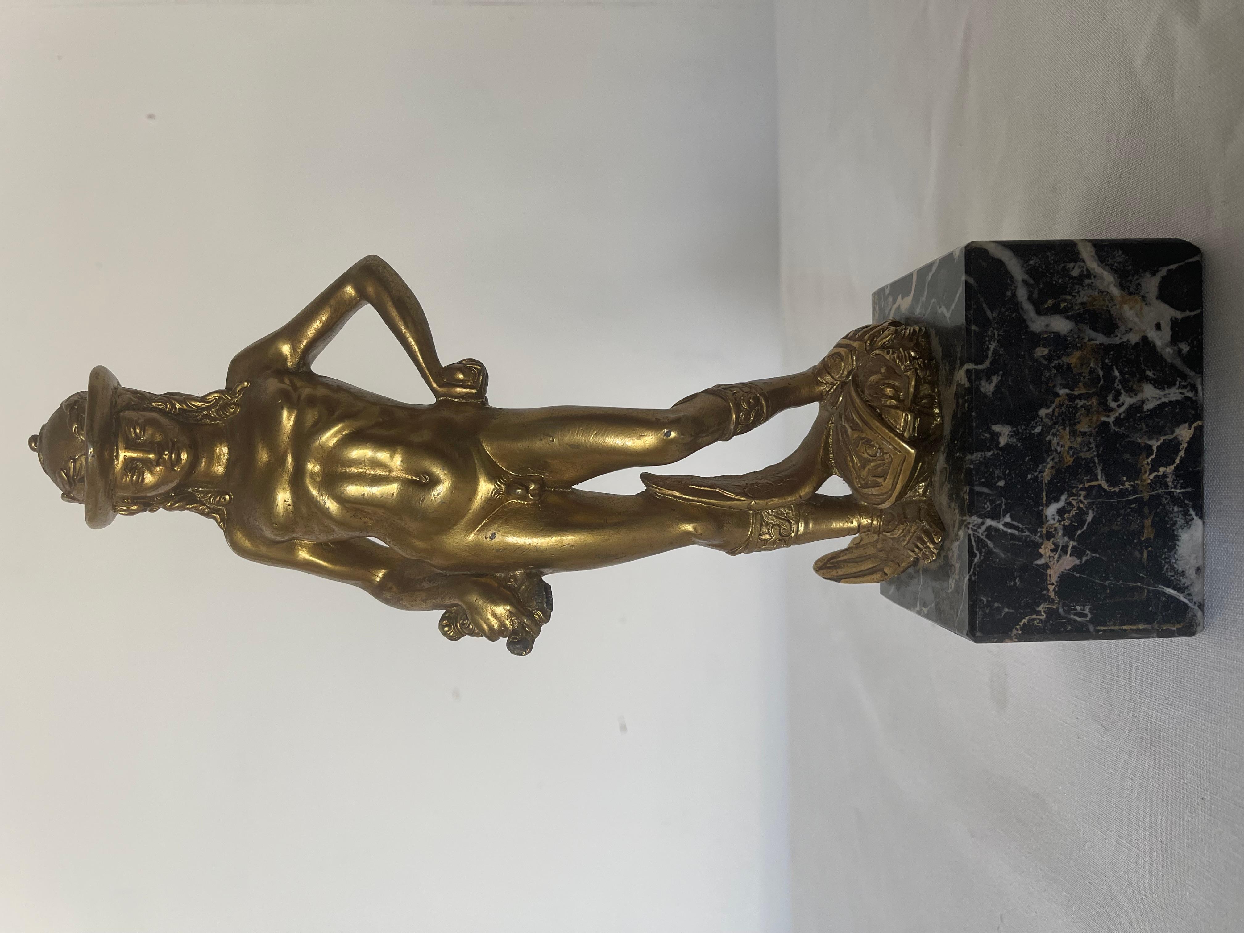 Elegante riproduzione del celebre David di Donatello, realizzata in bronzo dorato e montata su una solida base in marmo nero venato. La statua rappresenta il giovane David nell’iconica posa vittoriosa, con un'espressione fiera e rilassata, il piede