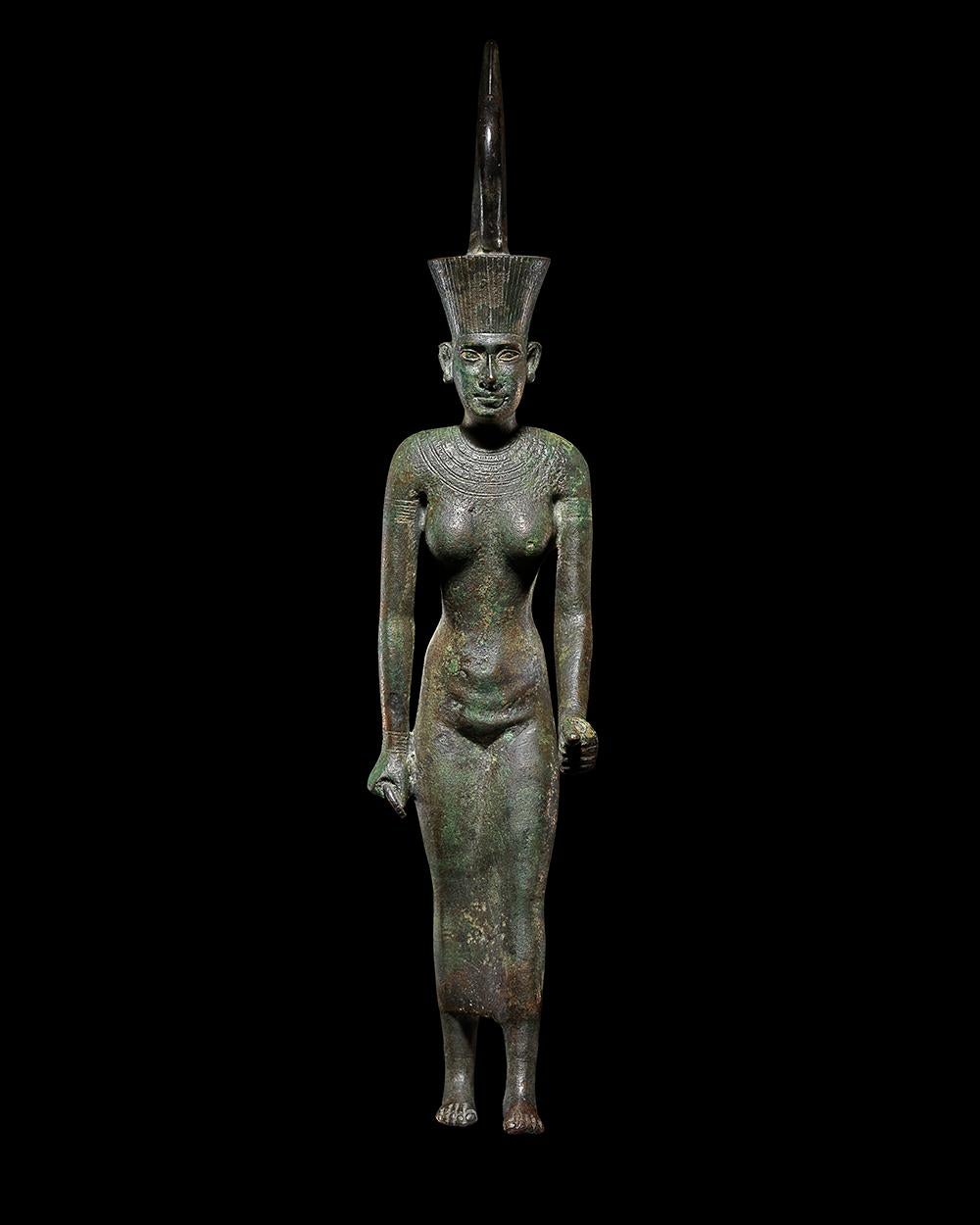 Bronze statue of the goddess Neith, striding, her left foot extended forward. Her left hand is extended forward and formally held a papyrus sceptre, a fragmentary ankh is visible in her right hand. She wears a close-fitting sheath dress, incised