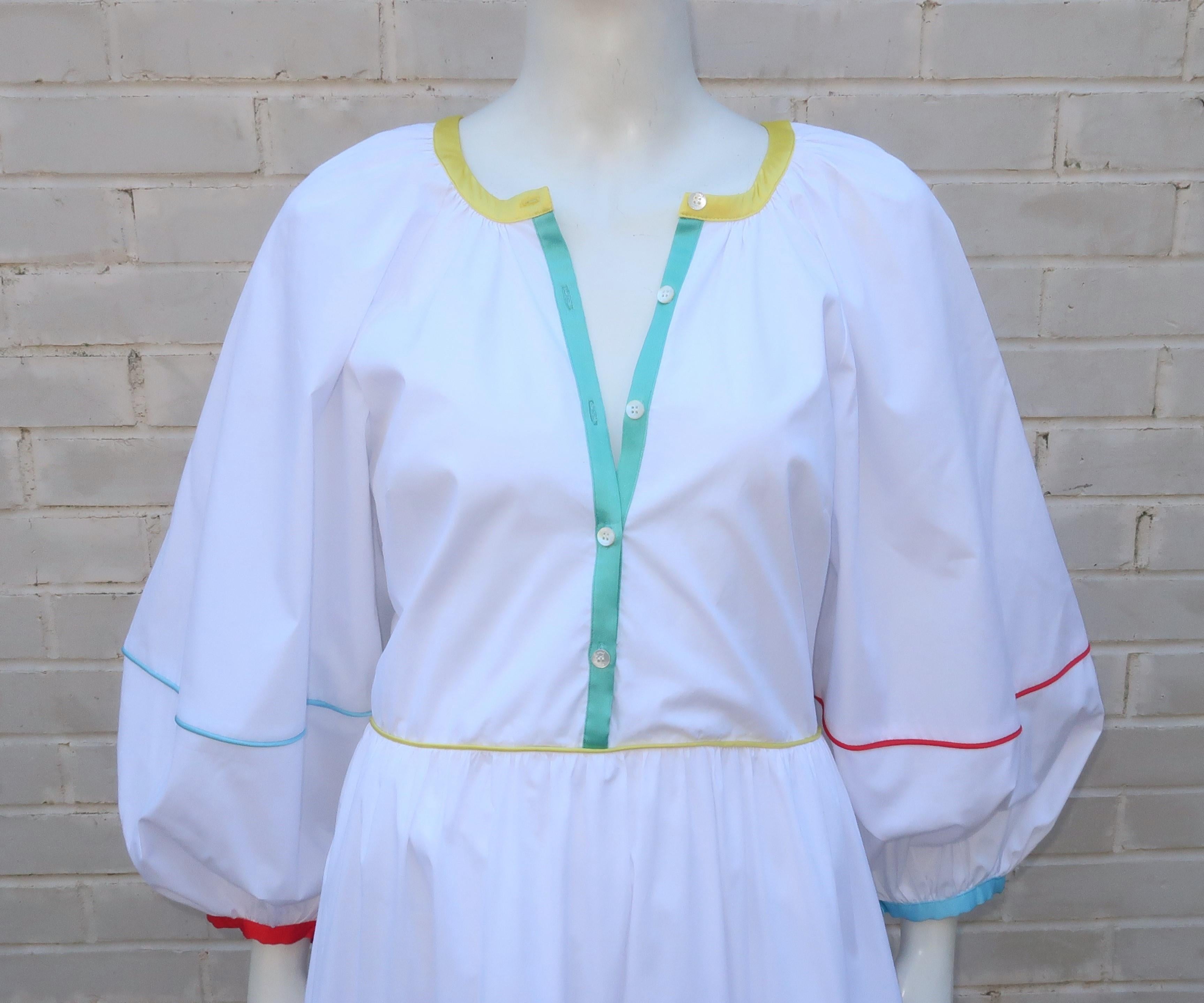 A flowing crisp white cotton maxi dress by Los Angeles based clothing company, Staud.  The dress has a vintage inspired peasant style with balloon sleeves and tiers accented by colorful satin cording including shades of yellow, orangey red, baby