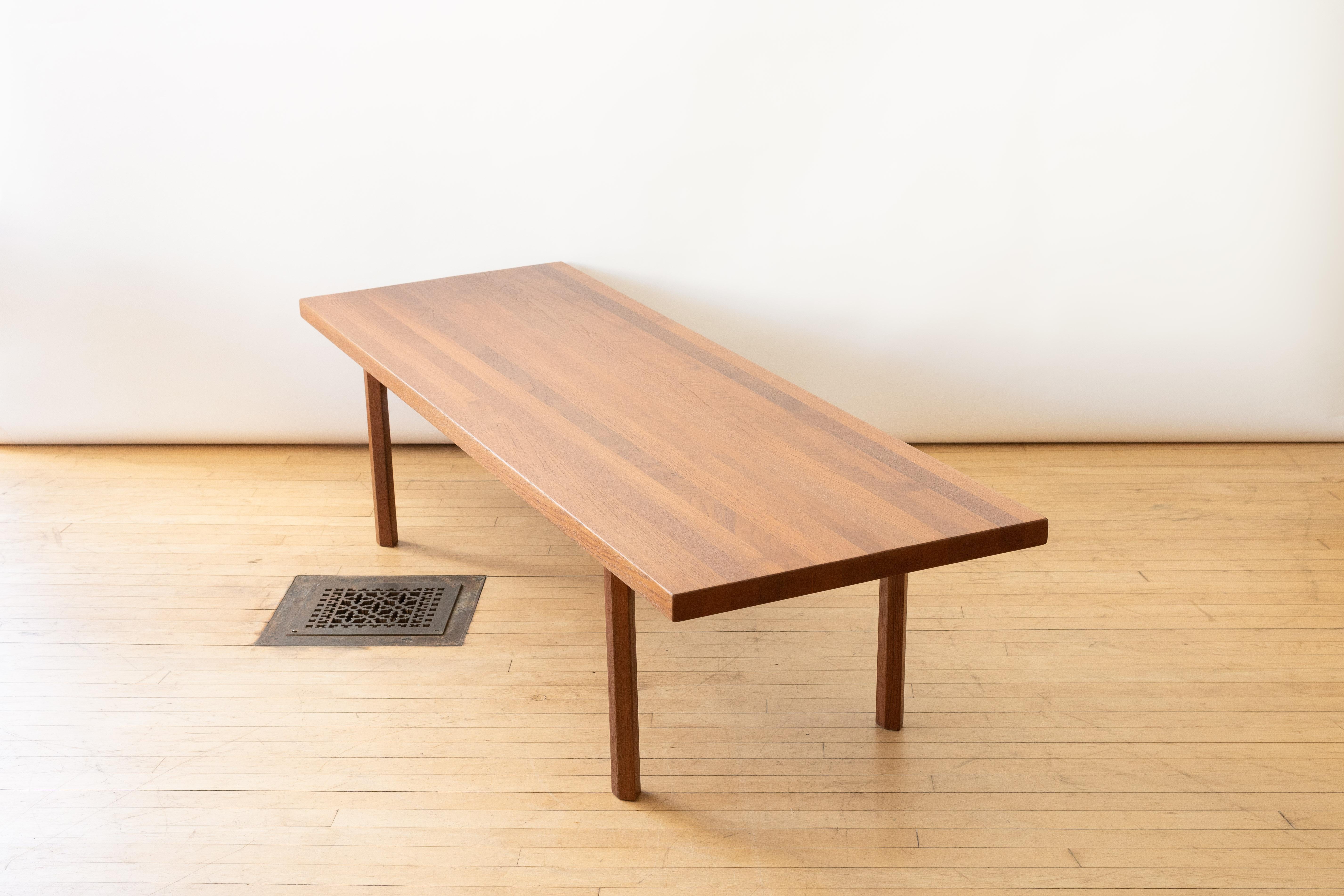 Danemark, vers les années 1960. Une grande table basse ou un banc incroyablement robuste, créée par Illum Wikkelsø pour A. Mikel Laursen. Le plateau rectangulaire en teck massif est soutenu par d'épais pieds chanfreinés. Parfaite pour une salle