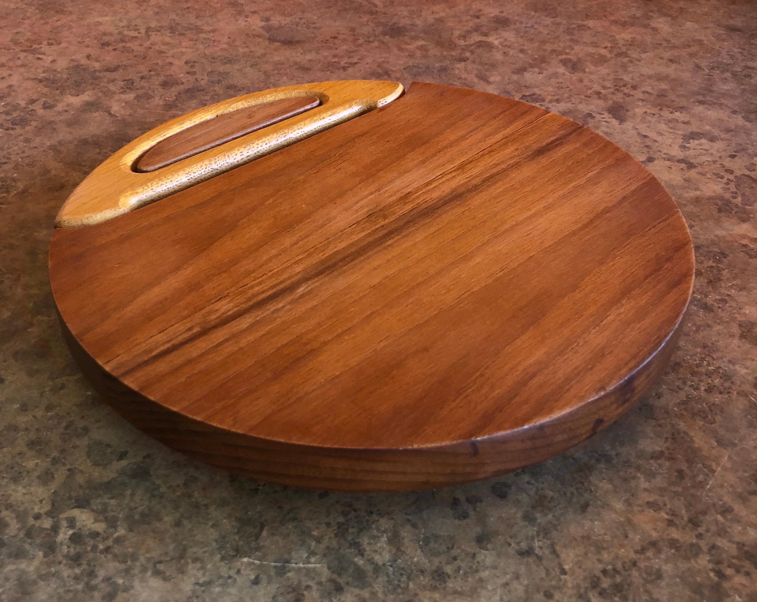 A pristine staved teak round cheese board with cutter by Jens Quistgaard for Dansk, circa 1950s. The board is 9.75