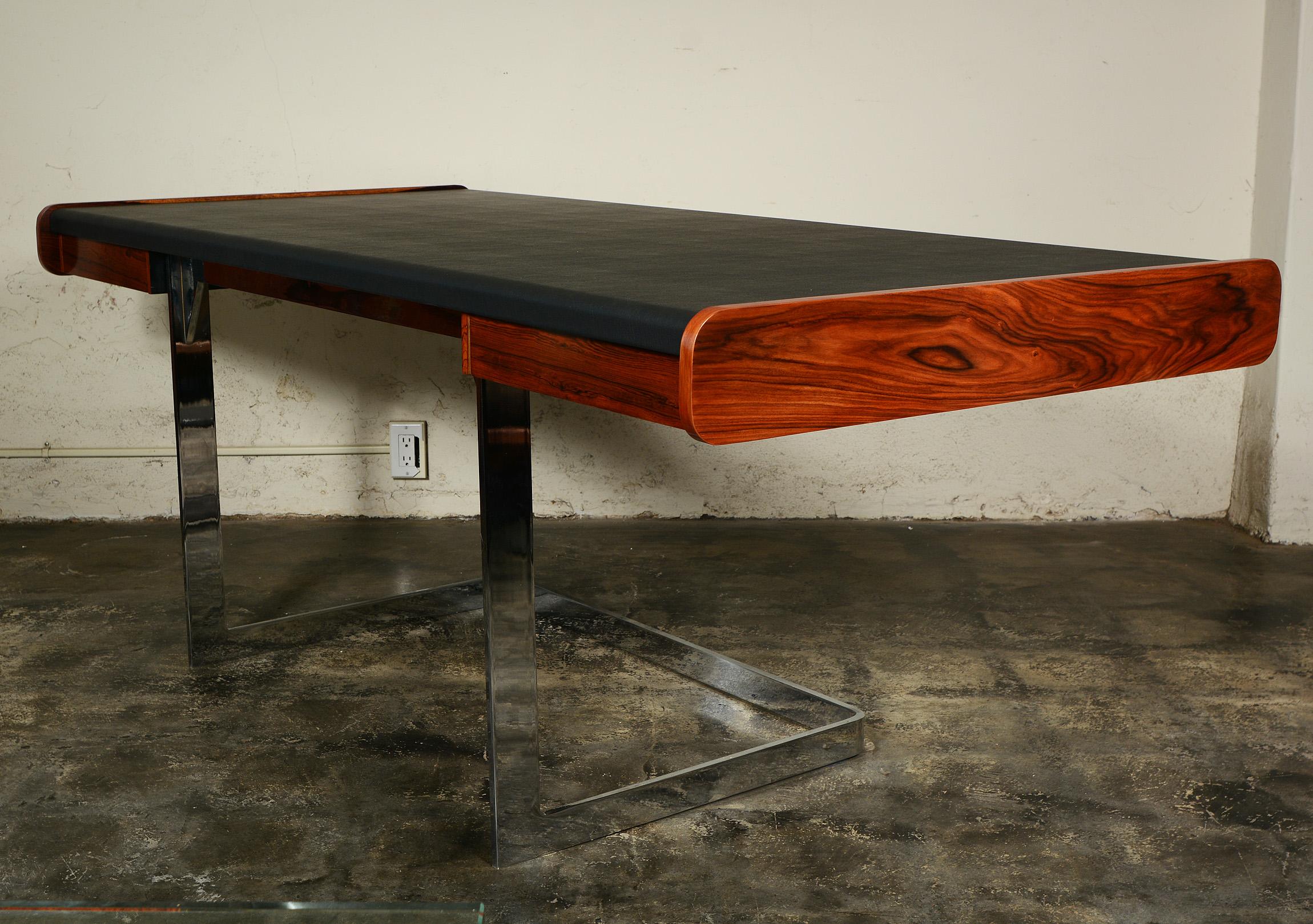 Sleek modernist desk by Ste. Marie and Laurent. The vinyl covered top rest on a cantilevered chrome base. There is a drawer on either side of the base. The drawers and ends are finished in rosewood. The desk is pictured without glides. We have