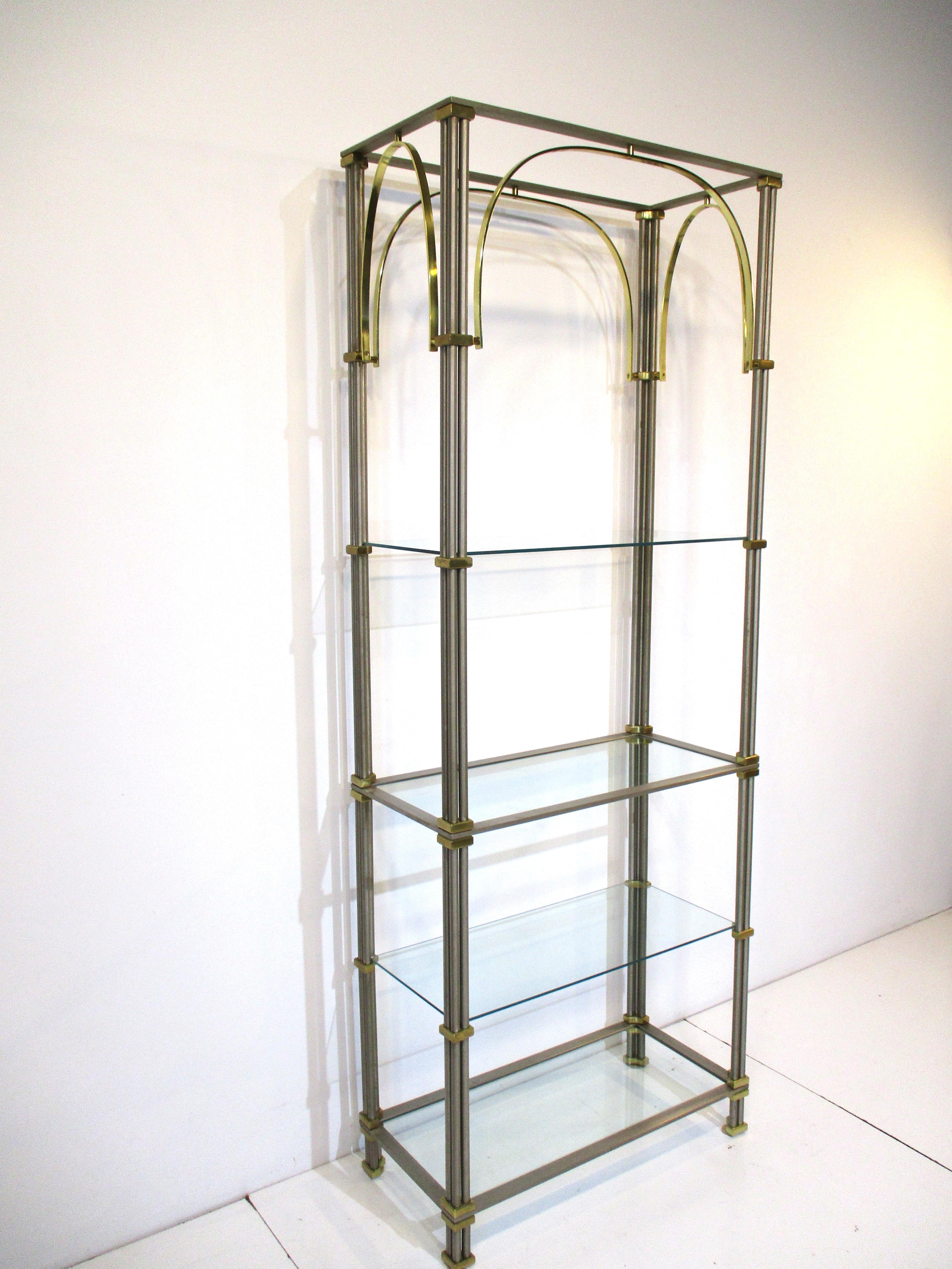 A brushed steel etagere having three heavy rods to each frame bound with brass details at each section with sweeping arched brass flat bar design to the upper structure. Four glass shelves to the piece, manufactured in the manner of Maison Jansen.