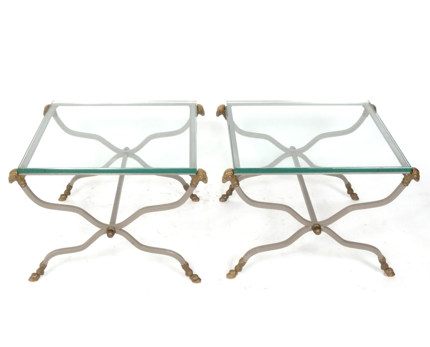Coppia di tavolini o comodini in stile Maison Jansen, francesi, circa anni '50. Costruito in acciaio con accenti in bronzo e piani in vetro. Le dimensioni sono versatili e possono essere utilizzate come tavolini o comodini. 