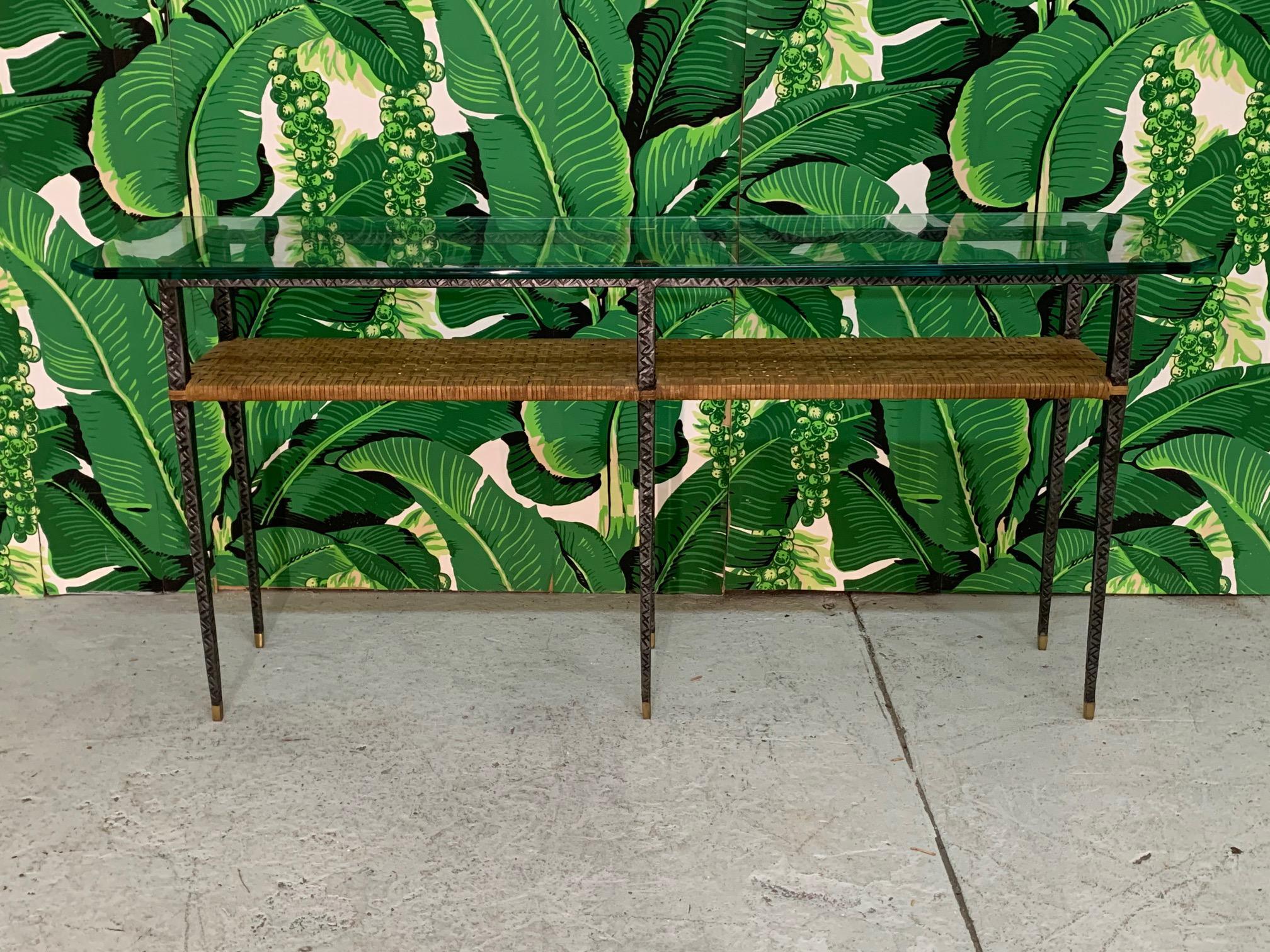 Mixed media console table features a metal frame with diamond cut detailing, brass accents, rattan center shelf, and a glass top. Very good condition with only very minor imperfections consistent with age. Glass top measures 60