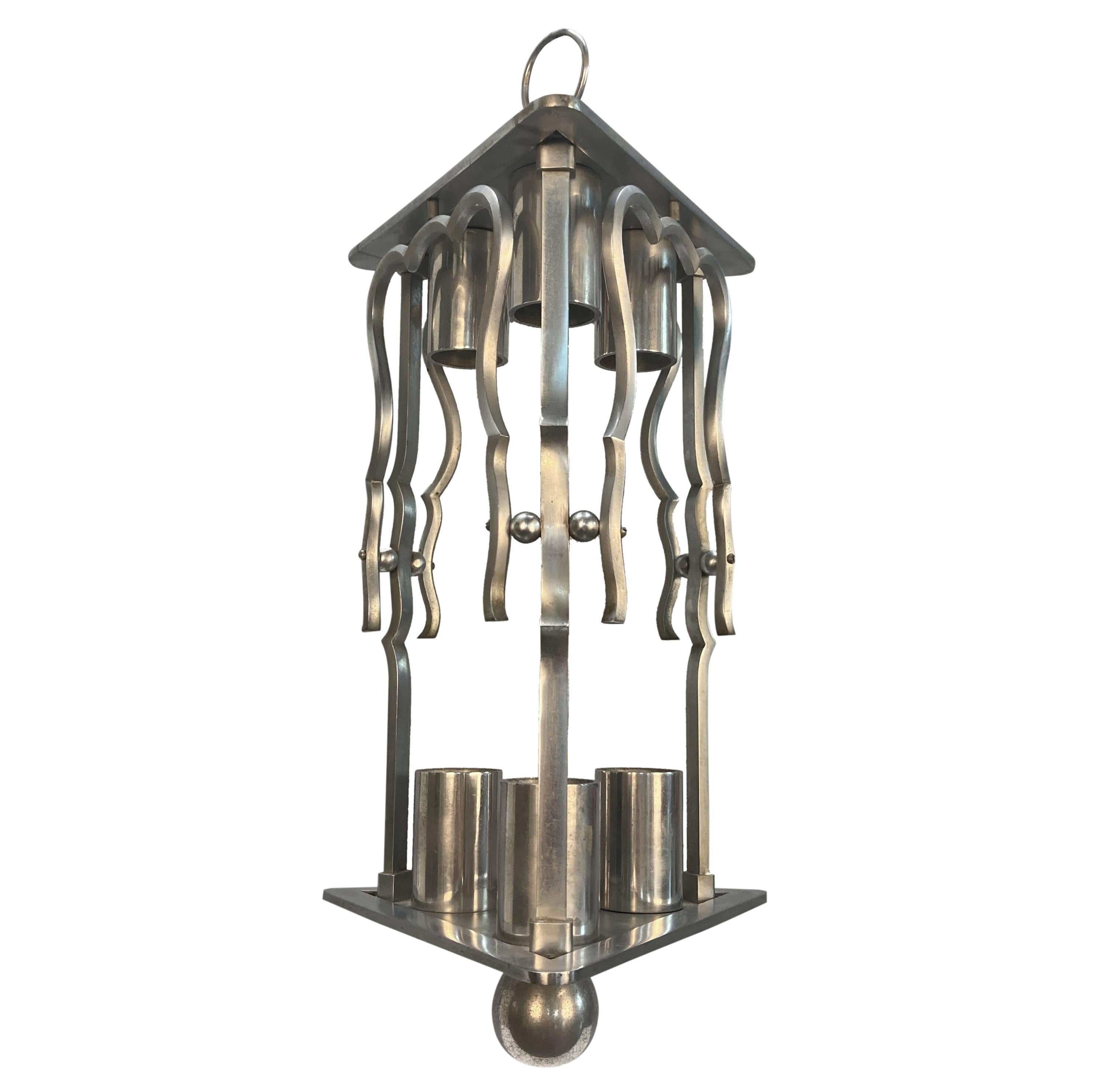 Lanterne française en acier poli. De forme triangulaire, elle est surmontée de trois lampes.