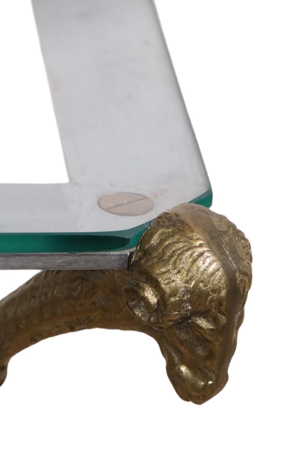 Insolite petite table en acier, laiton et verre attribuée à la Maison Jansen. La table comporte un plateau en verre à coins coupés (d'origine), des pieds et des têtes de sabots en laiton et un cadre en acier brossé. Cet exemple est plus petit que la