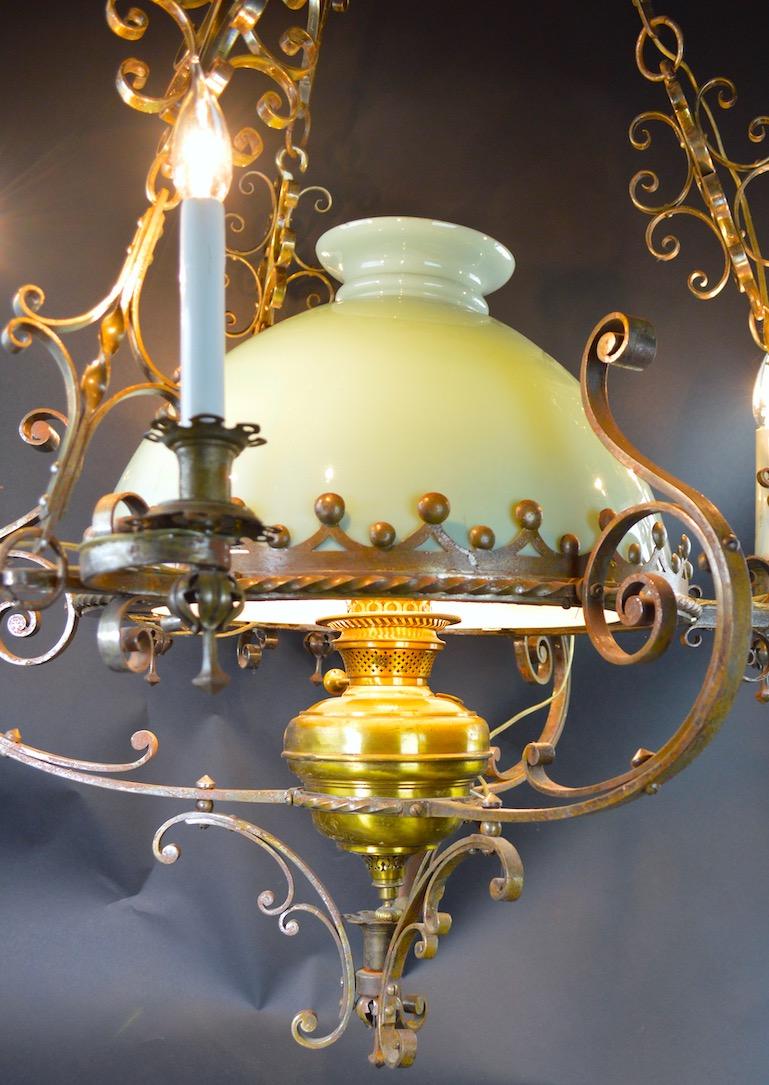 Very decorative wrought steel and brass frame hanging oil lamp chandelier, has been electrified for contemporary use. The metalwork is in the Spanish style, the shade is muted bluish green with cased white glass interior. Large and impressive 19th