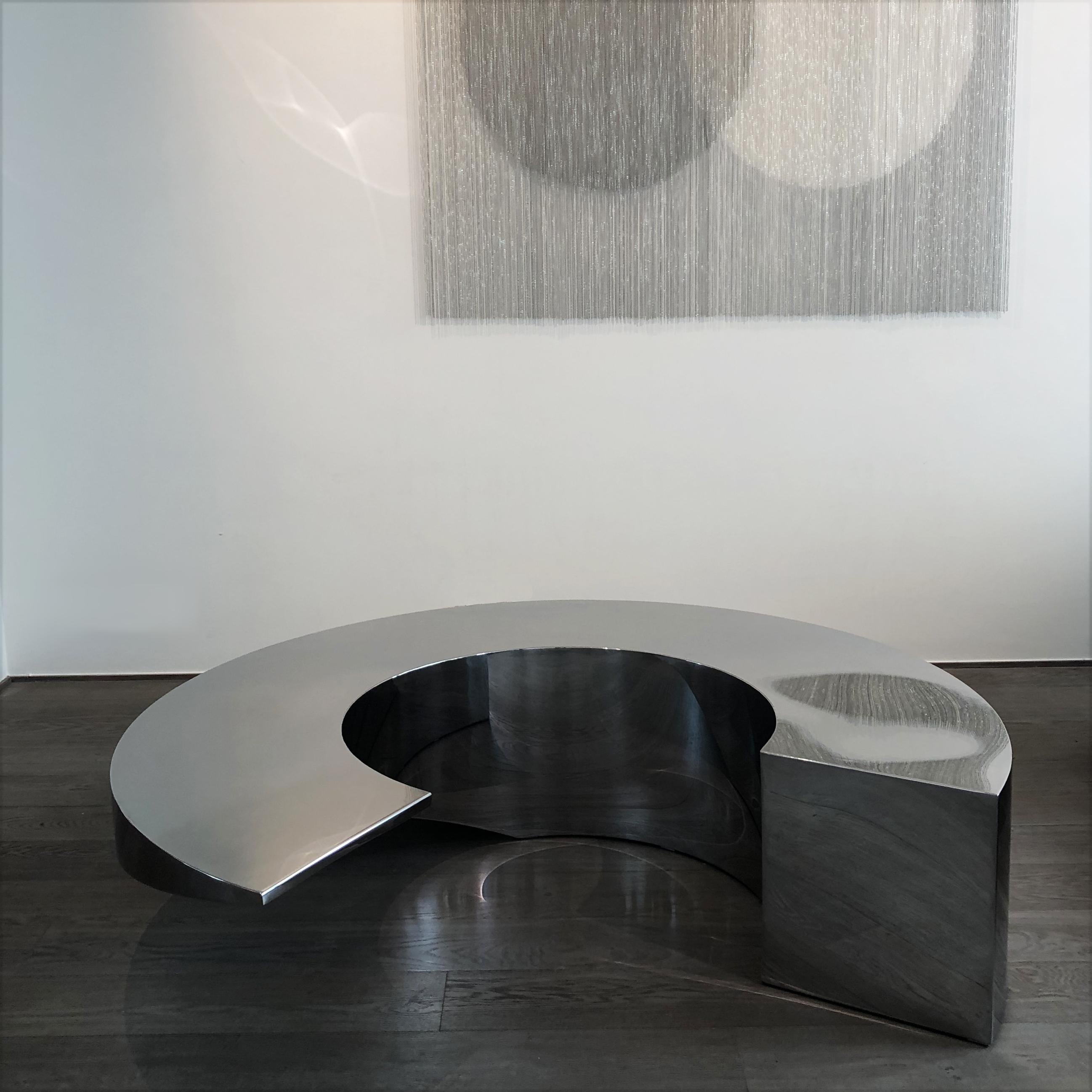 Table circulaire de Pol Quadens 
Édition limitée à 8+4 pièces.
Dimensions : Ø 150 x H 40 cm : Ø 150 x H 40 cm.
MATERIAL : Acier inoxydable poli miroir.

Pol Quadens est né à Bruxelles. Son père était actif dans les domaines des composites et de