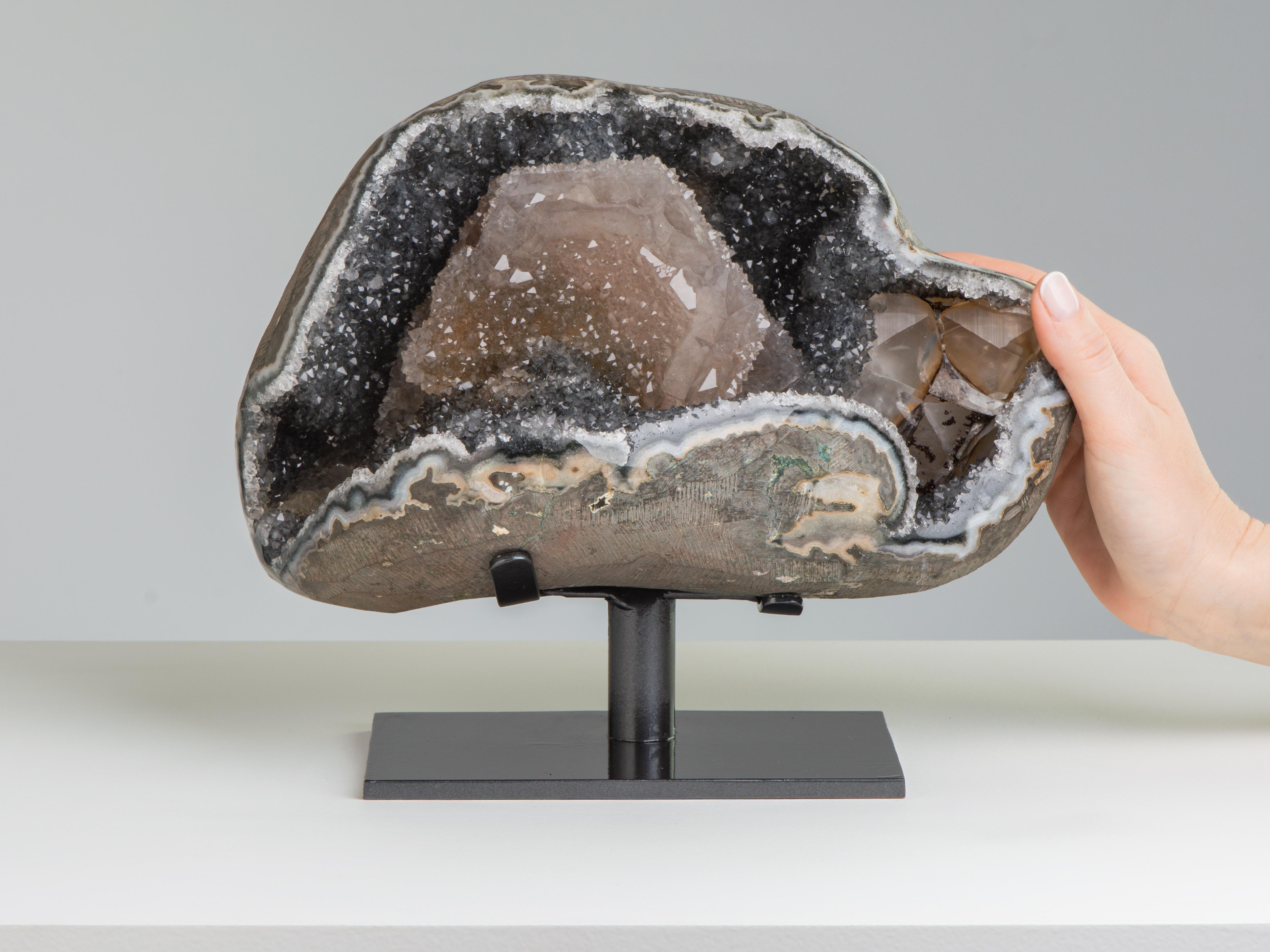 This open geode is lined with steel coloured quartz and embelished with a large central calite covered with tan coloured amethystine quartz. Several other calcites to the side.

Dimensions of stone: H 20cm x W 15cm x D 19cm.

