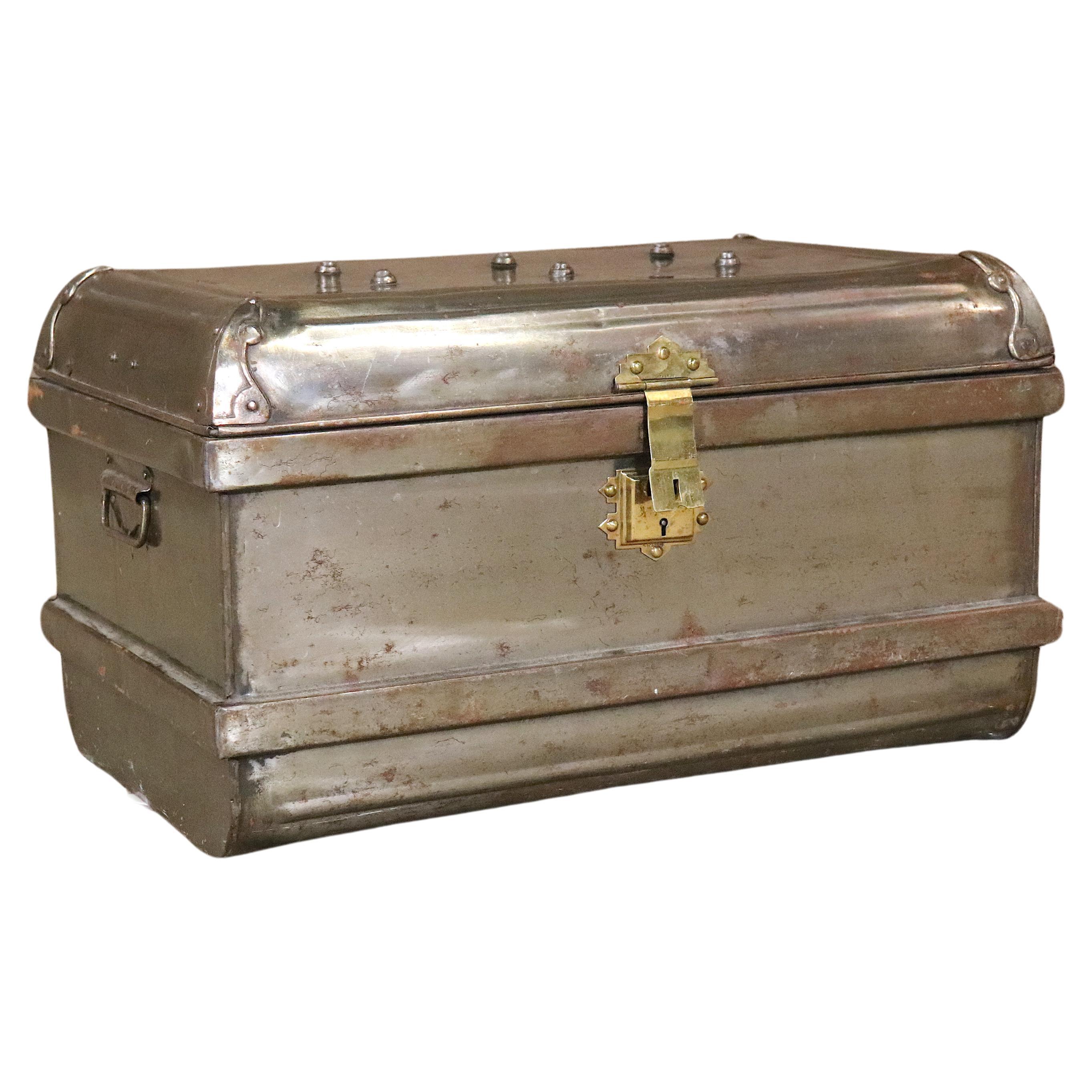 This industrial looking metal flip top trunk sports a brass latch, corner clamps, metal handles, rivets on the lid surface, painted black interior, and metal banding around the base and mid-section. Stylish storage solution for your modern home.