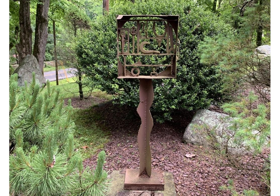 A garden sculpture by noted multidisciplinary artist Norma B. Flanagan. A tall piece, originally painted, now worn bare to a charming rust patina. With an openwork box at the top filled with various Found Iron objects including a wrench, horse shoe