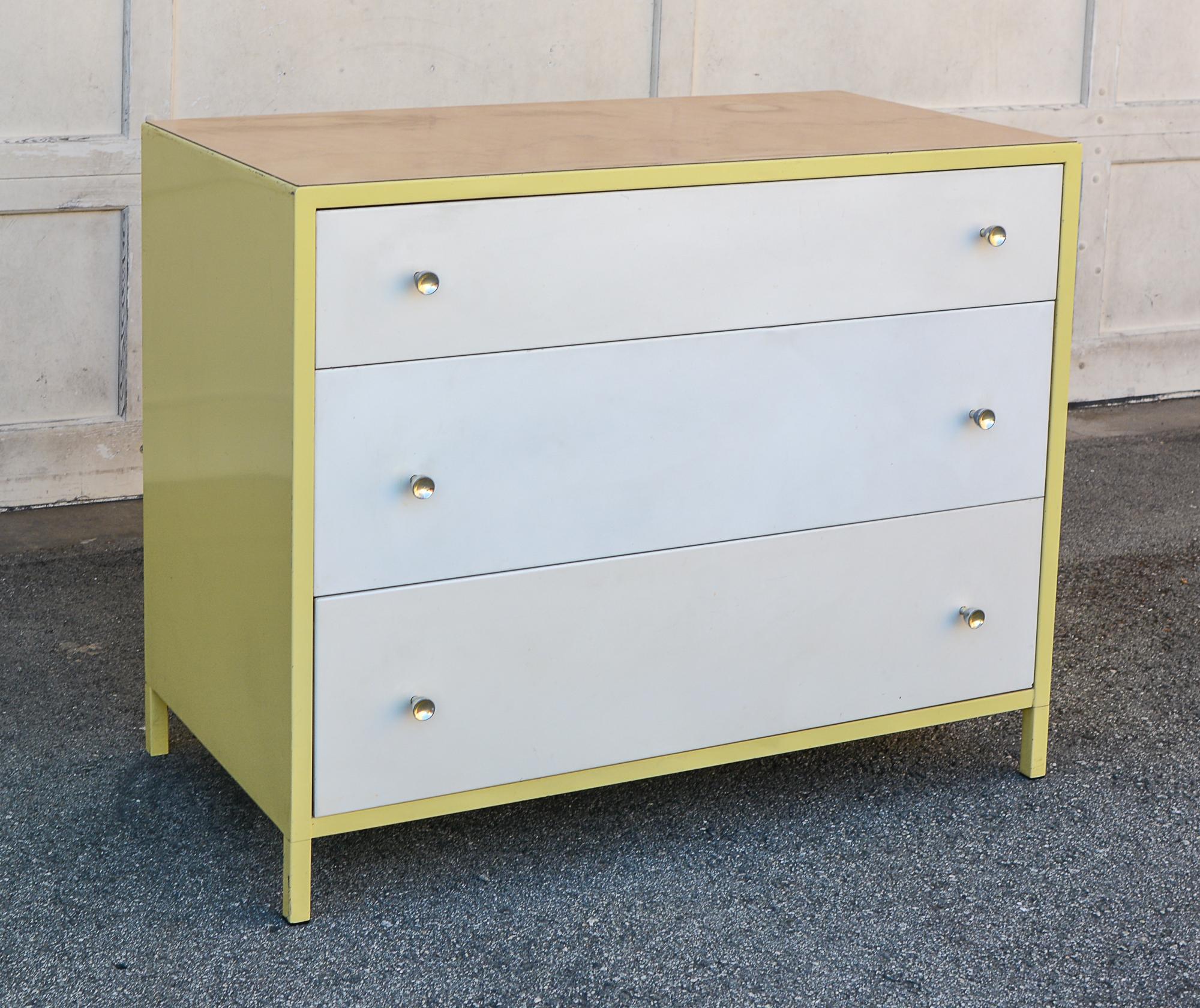 Steel dresser by Simmons Company from the Theme line. The dresser has a yellow case with white drawers. The top is a wood grain plastic laminate. There are some scratches and small paint losses. One drawer is a slightly different white than the