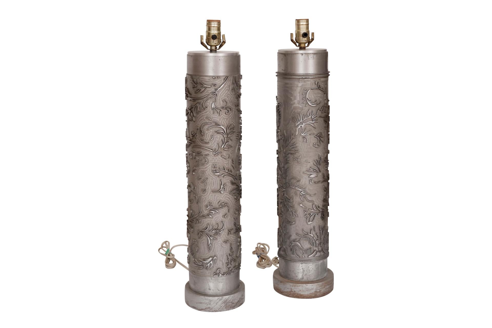 A tall pair of custom lamps made from steel wallpaper printing rollers. Decorated with a raised vine like pattern detailed with dots and lines. Each roller has a round wooden base. Dimensions per lamp.