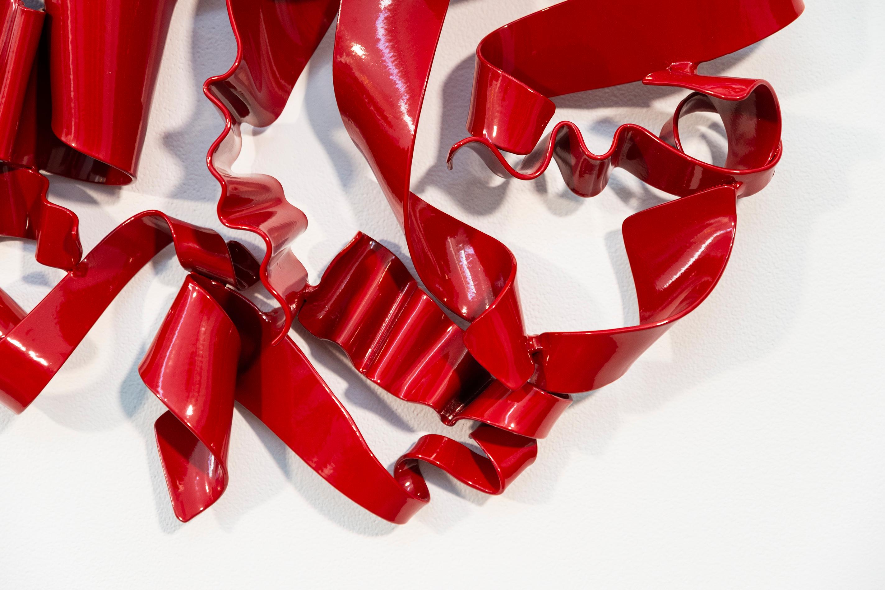 In a gorgeous candy coloured red, ribbons of steel swirl together curling and overlapping to form a circle. This is the dynamic work of Stefan Duerst.
The German born sculptor creates brightly coloured abstract sculptures from steel; their clean