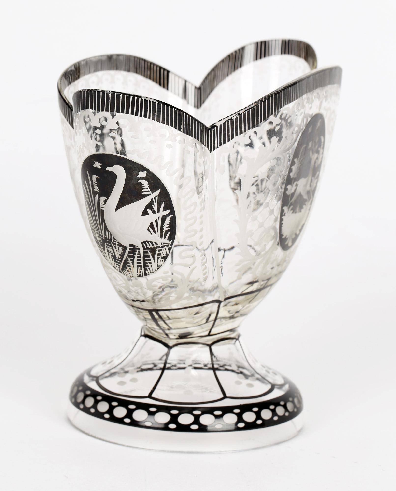 Stunning antique Bohemian pedestal glass vase with 'schwarzlot' designs and panels set amidst fine engraving and etching by Steinschönau and dating from the early 20th century. The vase stands raised on a wide rounded domed foot with a long three