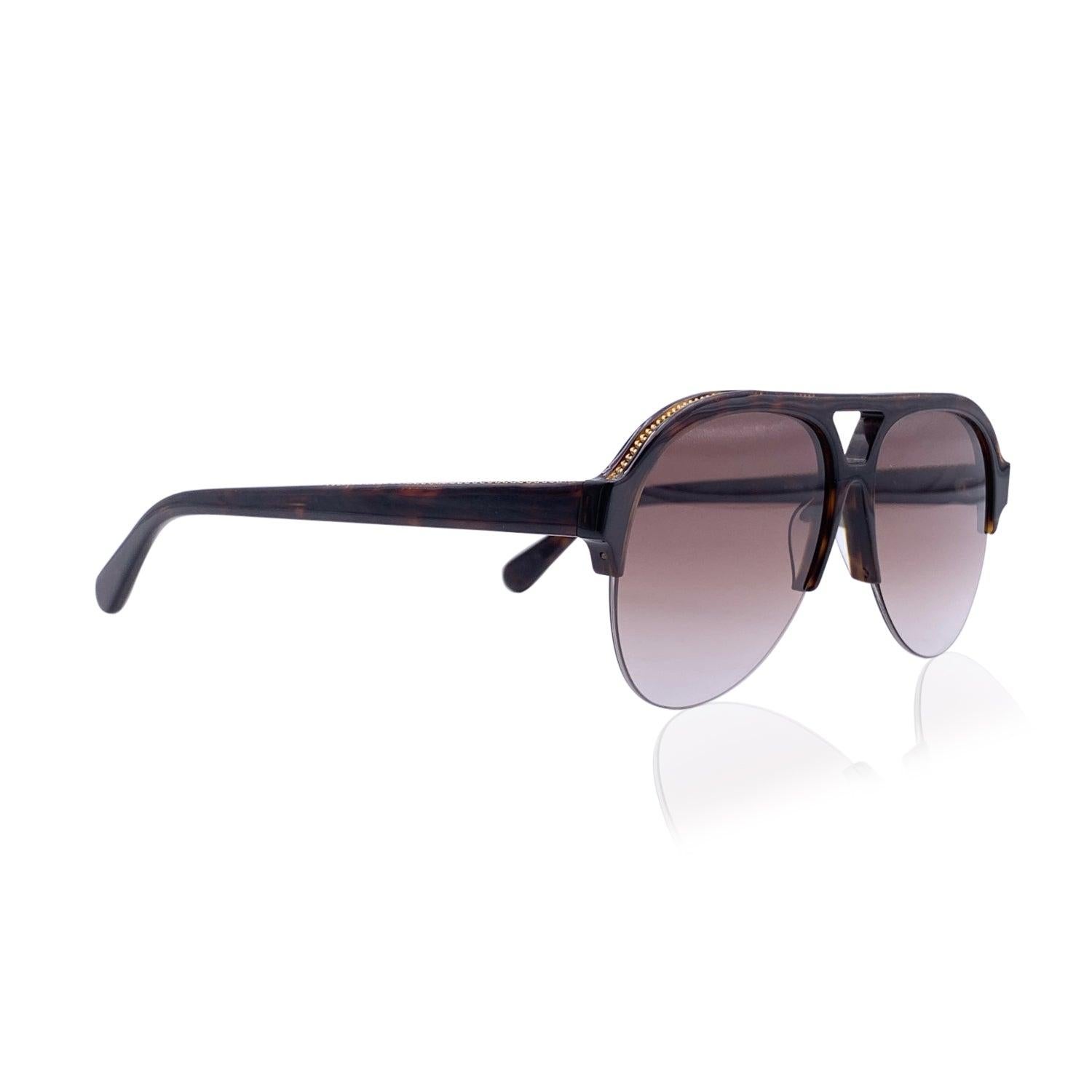 Stella McCartney aviator 'Falabella' sunglasses mod. SC0030S - c.002. They feature a half-rim brown frame in bio material. Gradient brown lenses. Gold metal chain detailing along the upper edges. Mod & refs.: mod. SC0030S - c.001 - 57/14 - 145. Made
