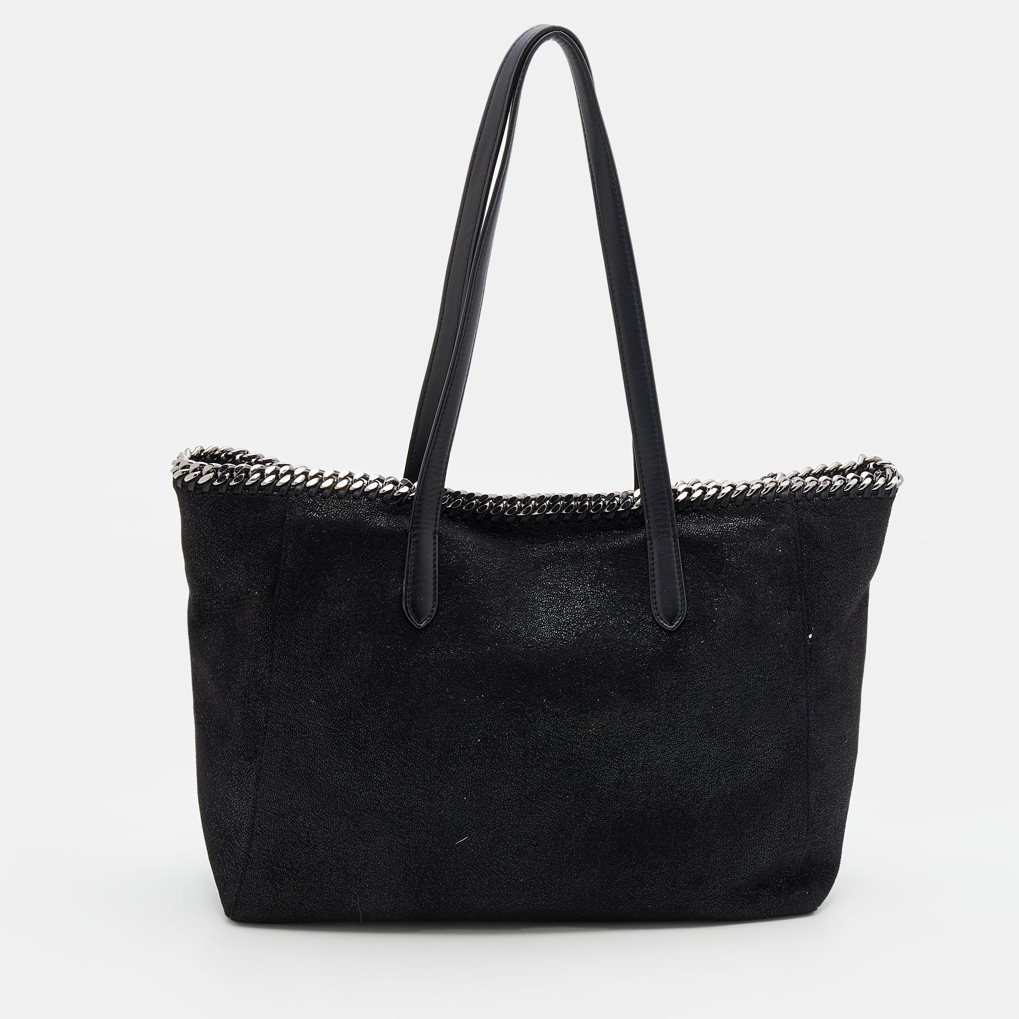 The iconic Falabella by Stella McCartney is presented as a shopper tote. The stunning creation has a black faux leather exterior embellished with metal chain detailing and dual straps. A spacious fabric interior completes it. This tote is going to
