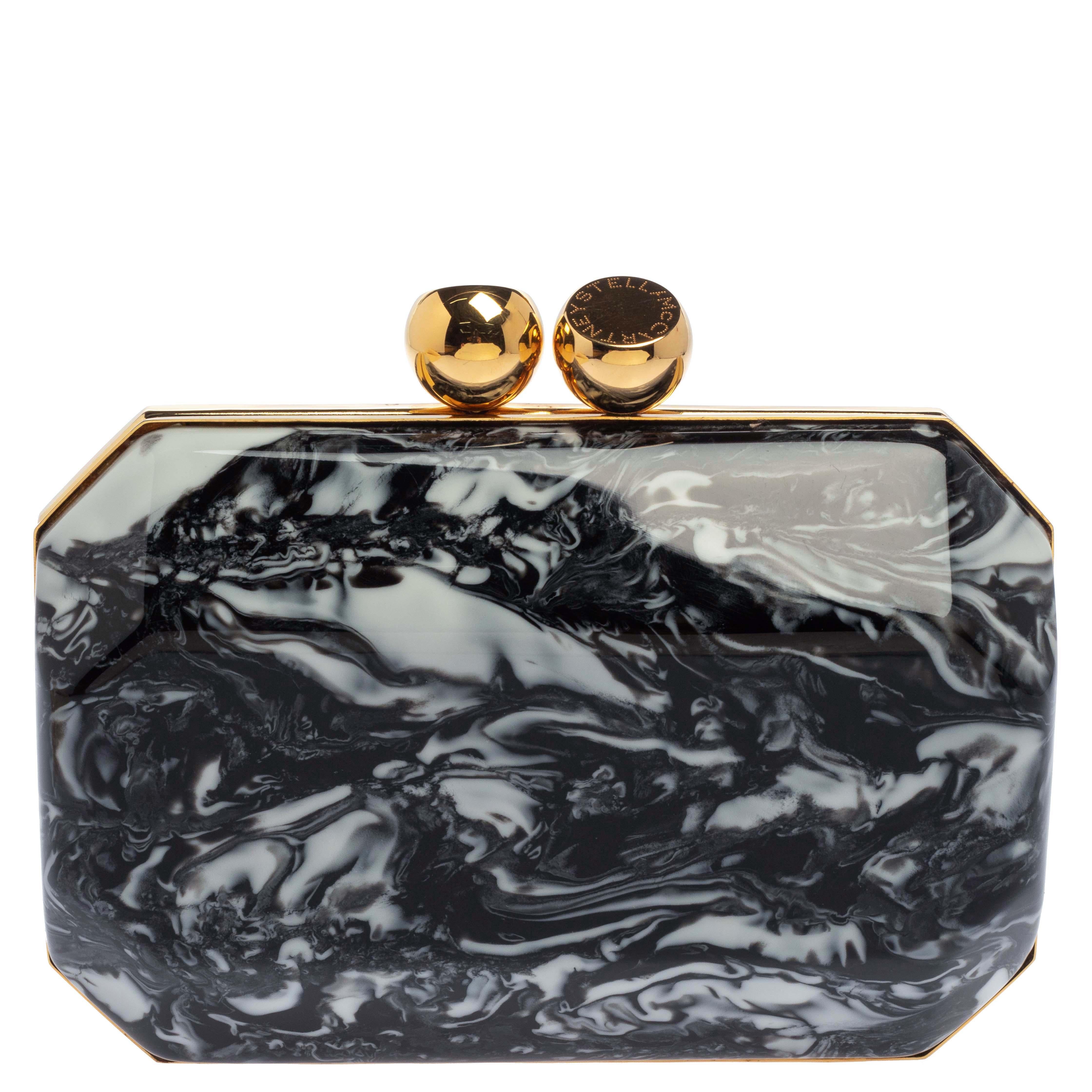 Fierce, funky, and eye-catching, this Stella McCartney Lucia clutch is perfect for a fun night out. Its stylish plexiglass exterior is adorned in black and white hues and is designed in an unusual geometric shape with gold-tone outlines and kiss