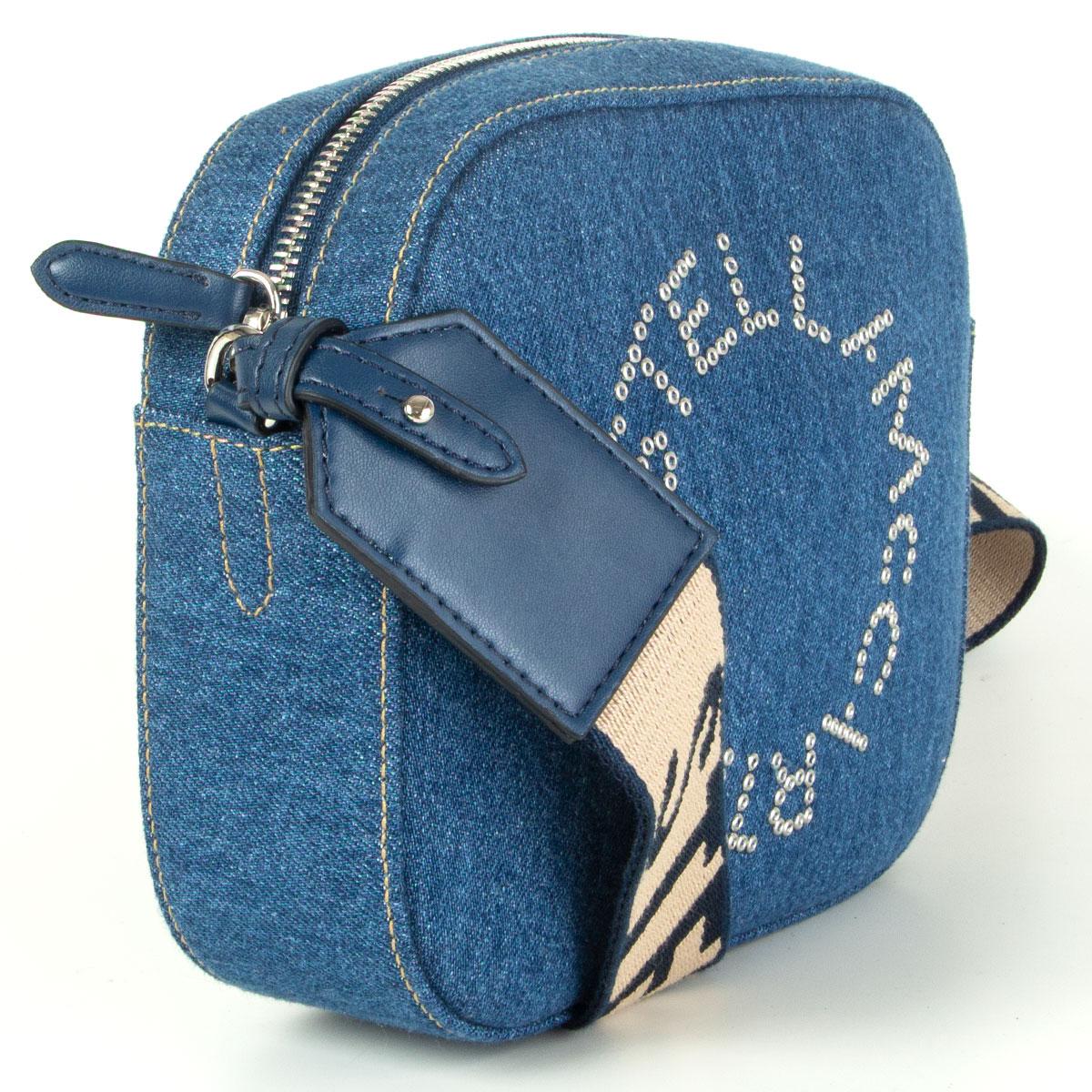 Stella McCartney denim logo mini camera bag in indigo cotton with faux leather details and an adjustable beige and navy blue logo shoulder strap. Open with a zipper on top and is lined in tan microfibre with one open pocket against the back. Brand