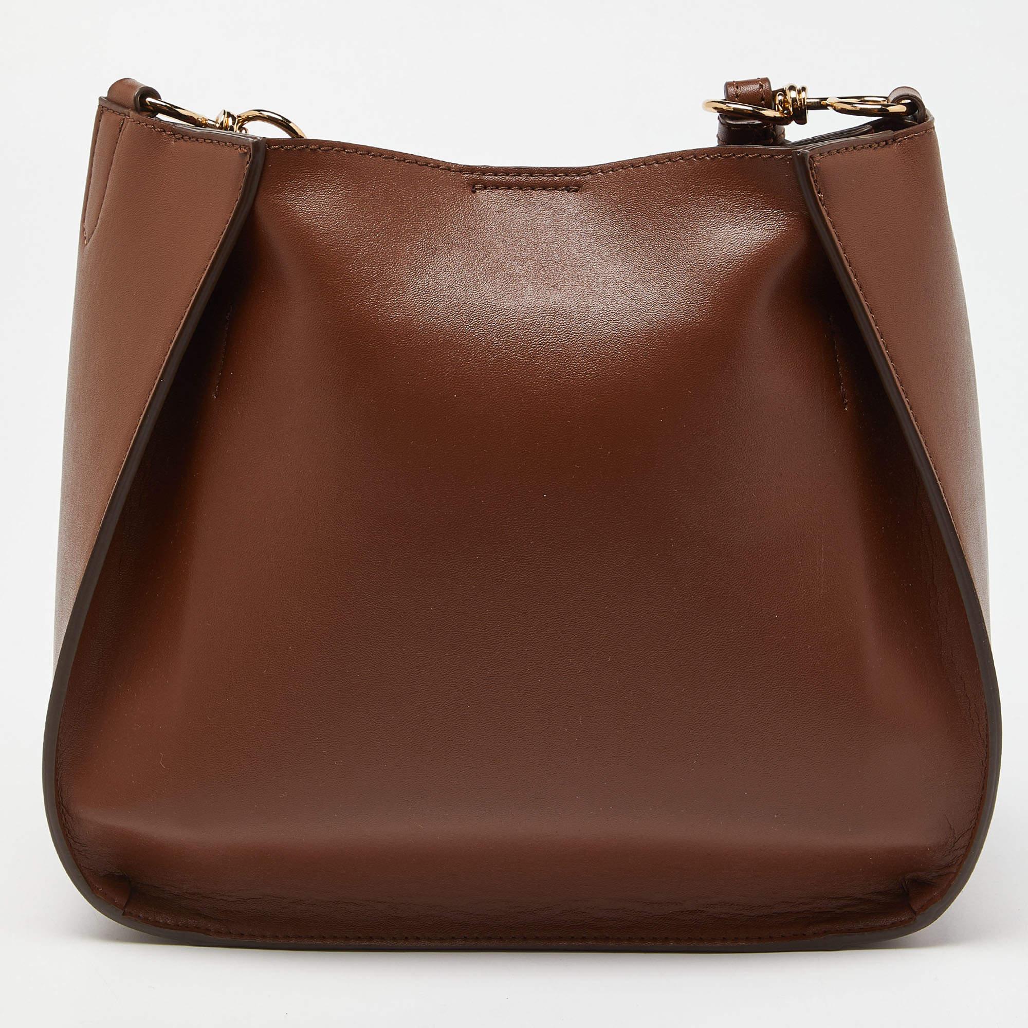 This crossbody bag from the House of Stella McCartney offers eternal style, luxury, and functionality. It is crafted using brown faux leather, with logo detailing highlighting the front. It exhibits an Alcantara-lined interior, gold-tone hardware,