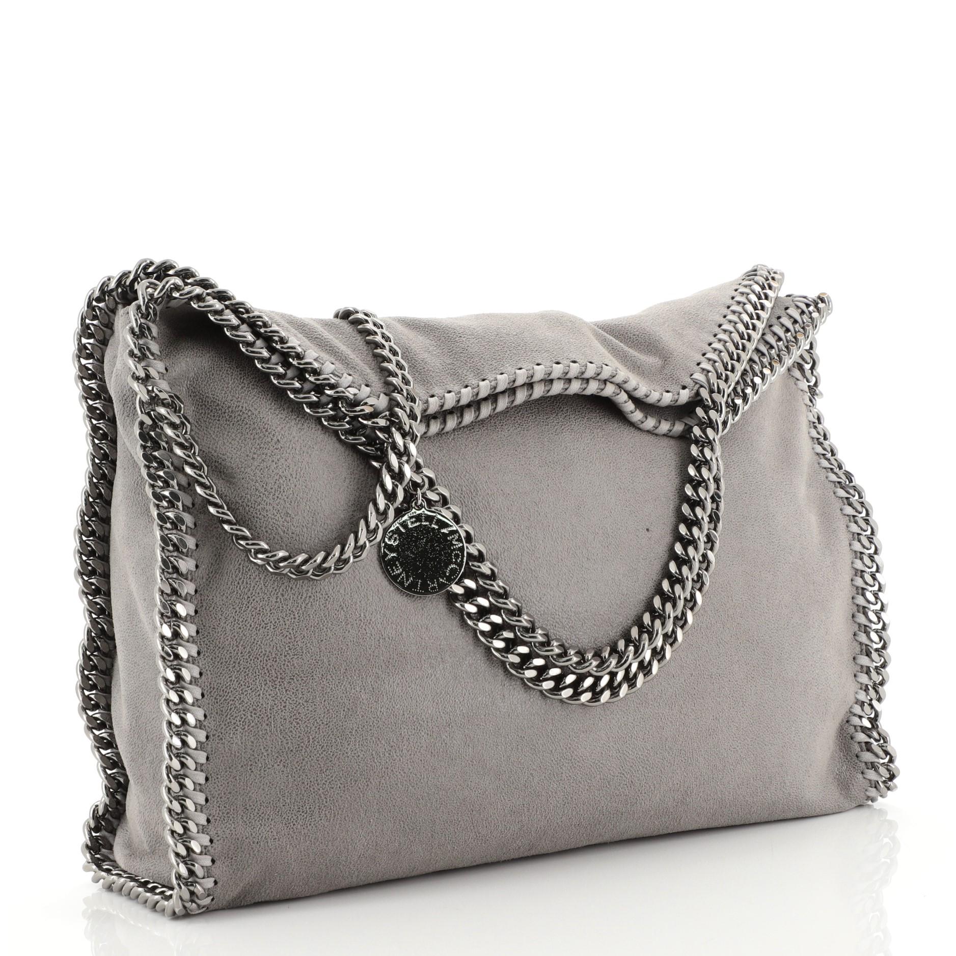 This Stella McCartney Falabella Fold Over Bag Shaggy Deer, crafted from gray shaggy deer, features chain link handles and trim, whipstitched edges, hanging logo disc, and gunmetal-tone hardware. Its magnetic snap closure opens to a pink fabric