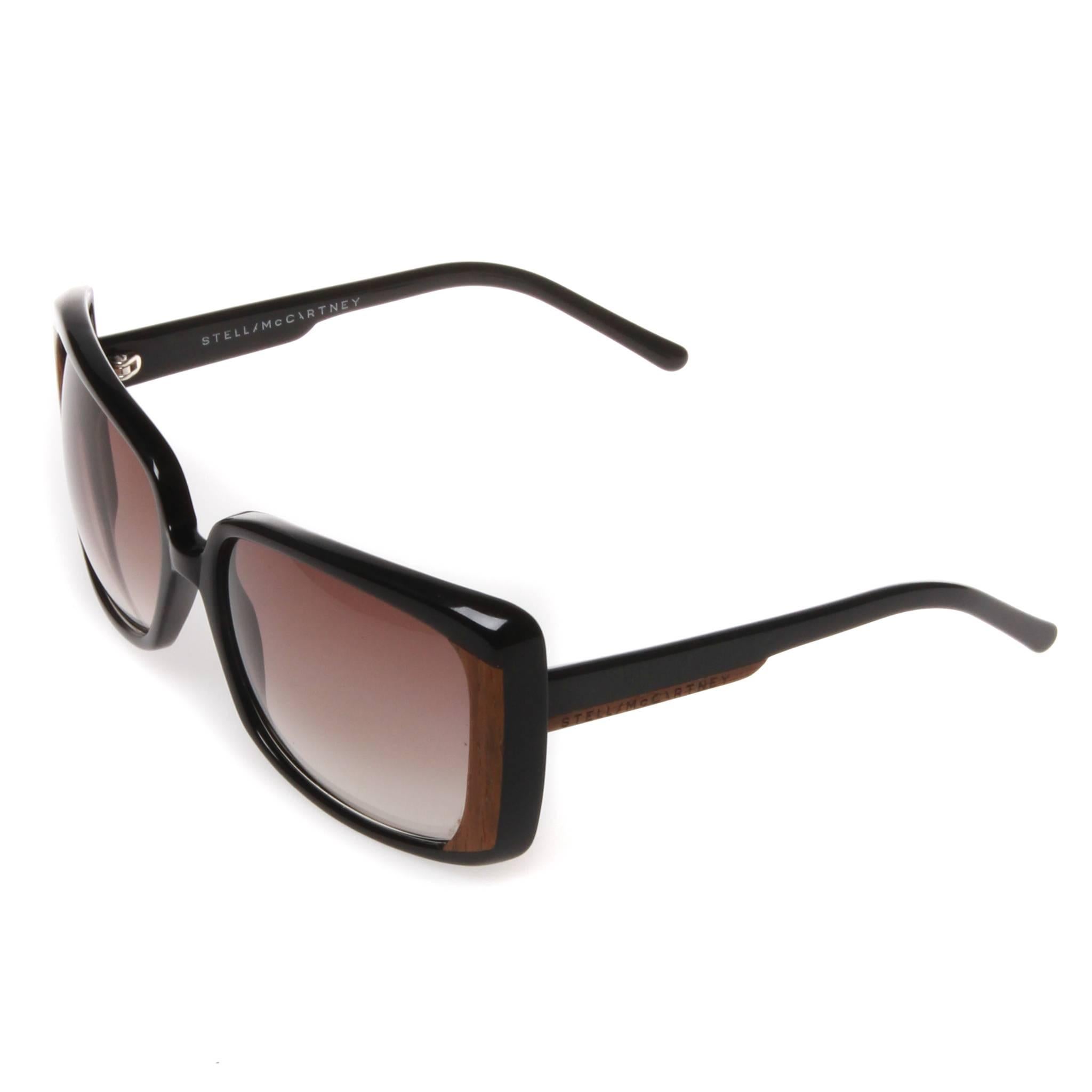 A pair of square set oversized Stella McCartney sunglasses featuring wooden detailing on the outer lens-side and engraved with the brand name on both arms. Frame is gloss black with lenses in a light gradient. Comes with authentic box.
