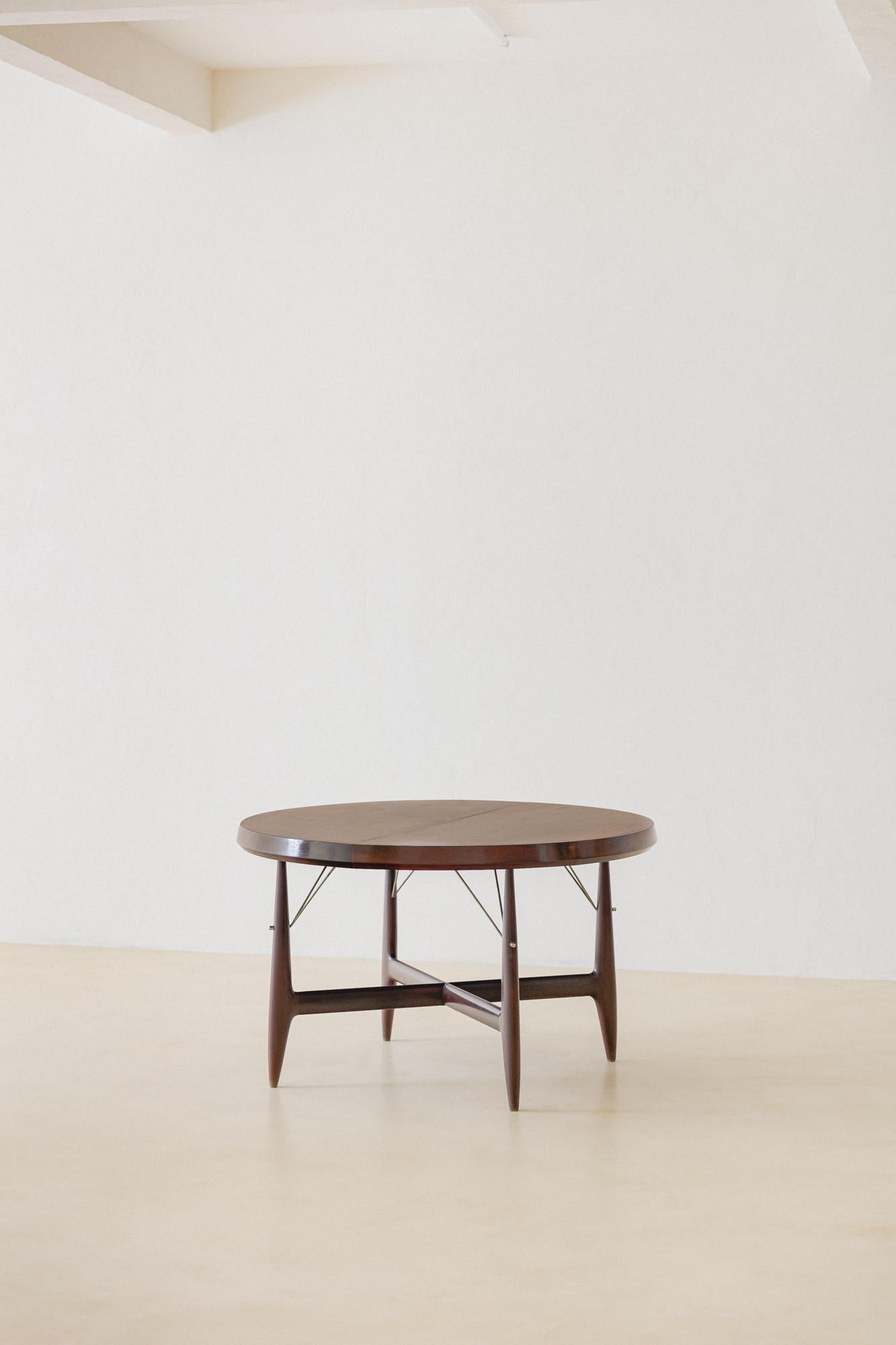 This expandable table is an example of the inventive designs by Sergio Rodrigues (1927-2014). The four-seat table made of solid Rosewood with a veneered top is extendable for six seats, with a practical engine at the table's center. 

This piece