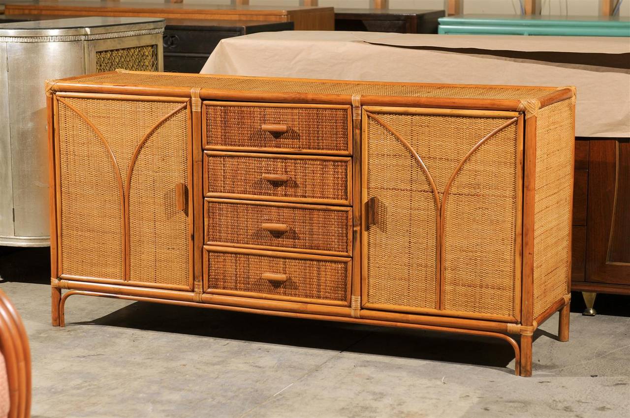 A beautiful rattan and cane cabinet or buffet, circa 1970s. Exceptionally crafted mahogany and rattan case construction with cane veneer and bamboo accents. The multipurpose design offers a center bank of drawers flanked by two open compartments.