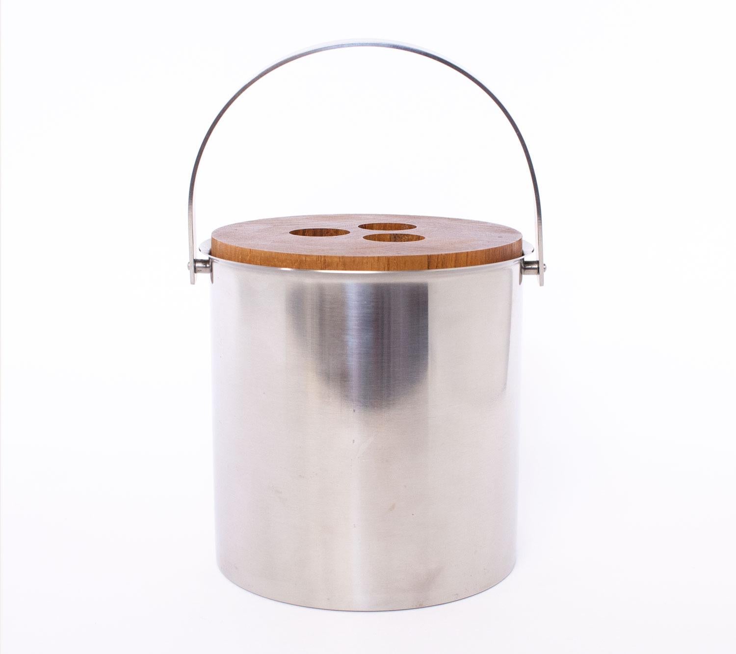 1960s Danish  ice bucket designed by Arne Jacobsen for Stelton.  The round stainless steel bucket contains a black plastic liner and it has teak lid with distinctive bowling ball style handles.