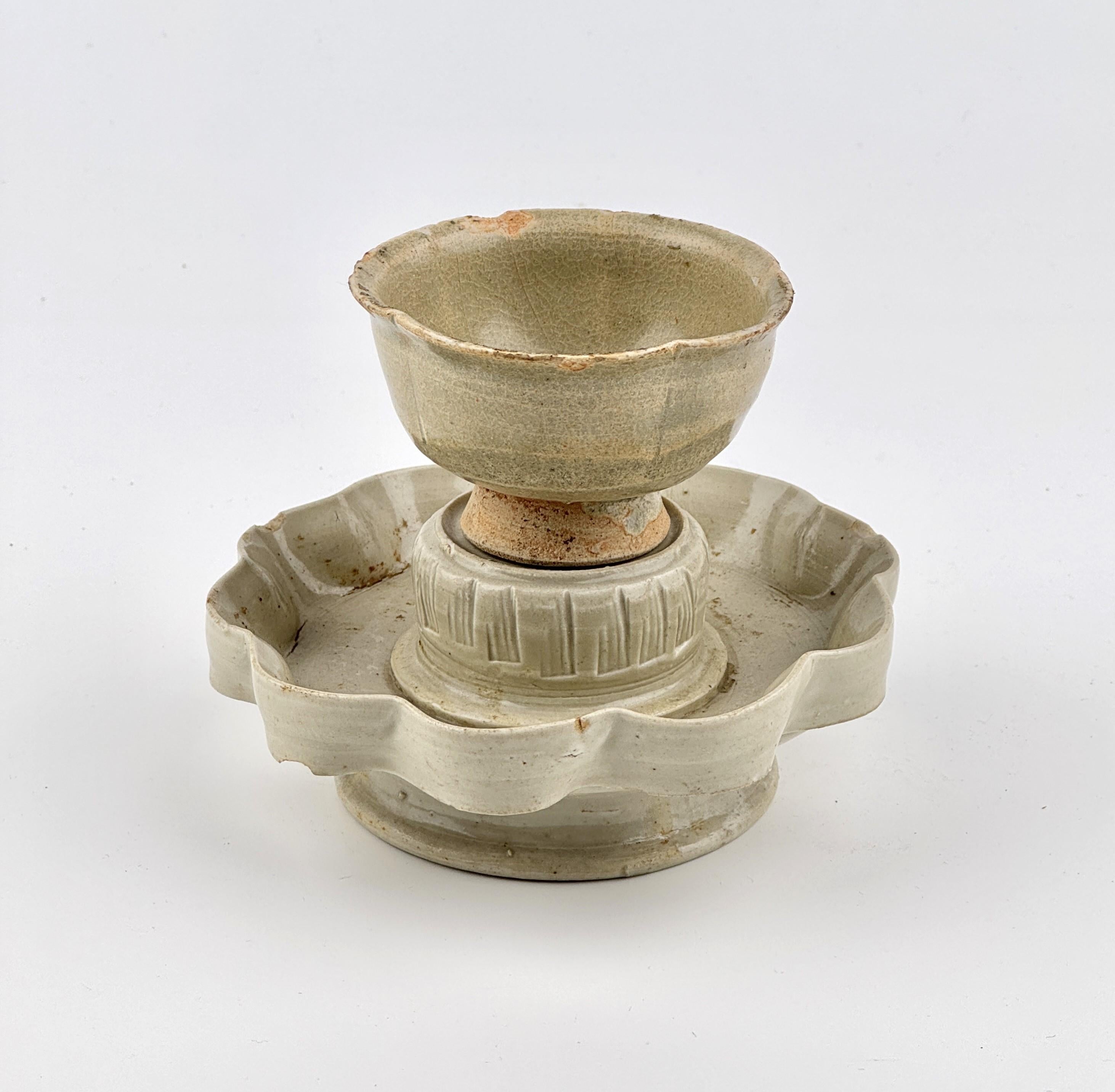 Five-lobed cup, featuring a delicate rim, is supported by a short, gently spreading foot. The accompanying stand rises elegantly from a broad base to a plate with an elevated, foliate-edged rim. The interior showcases a flower-head-shaped cup stand