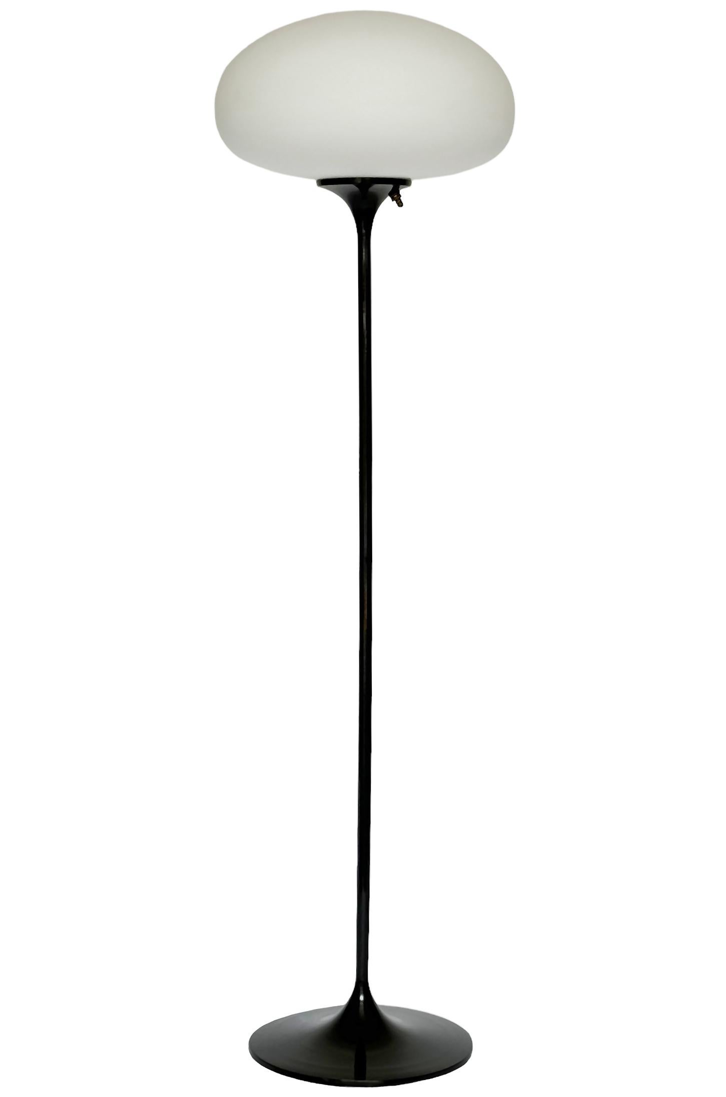 Ein schlanker, flacher Boden von Design-Line. Sie verfügt über einen Aluminiumguss-Sockel in einer skulpturalen Tulpenform. Der Sockel ist in sattem Schwarz glänzend ausgeführt. Die Lampe aus mattiertem Glas ist mundgeblasen und gibt ein weiches,