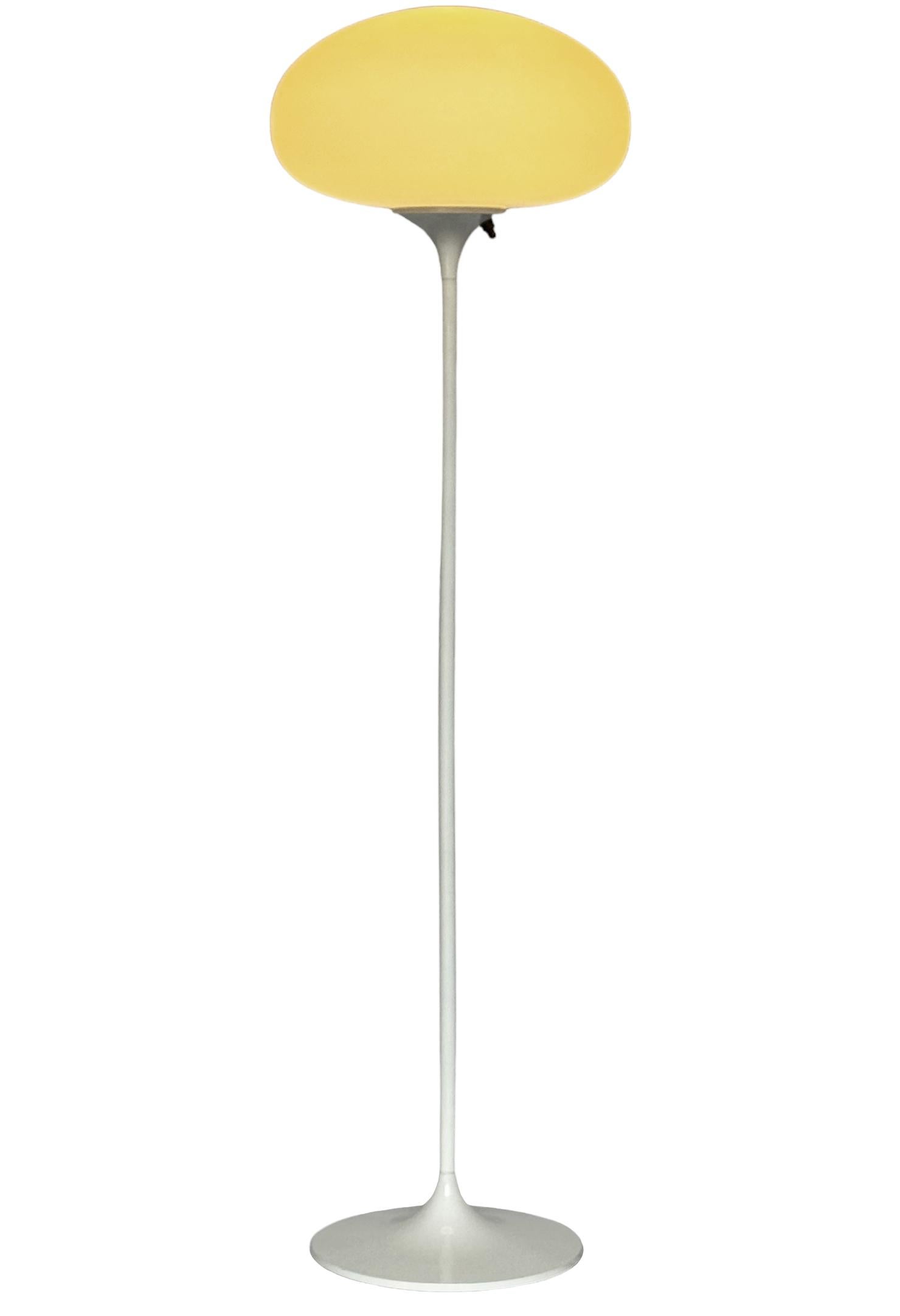 Ein schlanker, flacher Boden von Design-Line. Sie verfügt über einen Aluminiumguss-Sockel in einer skulpturalen Tulpenform. Der Sockel ist in klassischem Hochglanzweiß gehalten. Die Lampe aus mattiertem Glas ist mundgeblasen und gibt ein weiches,