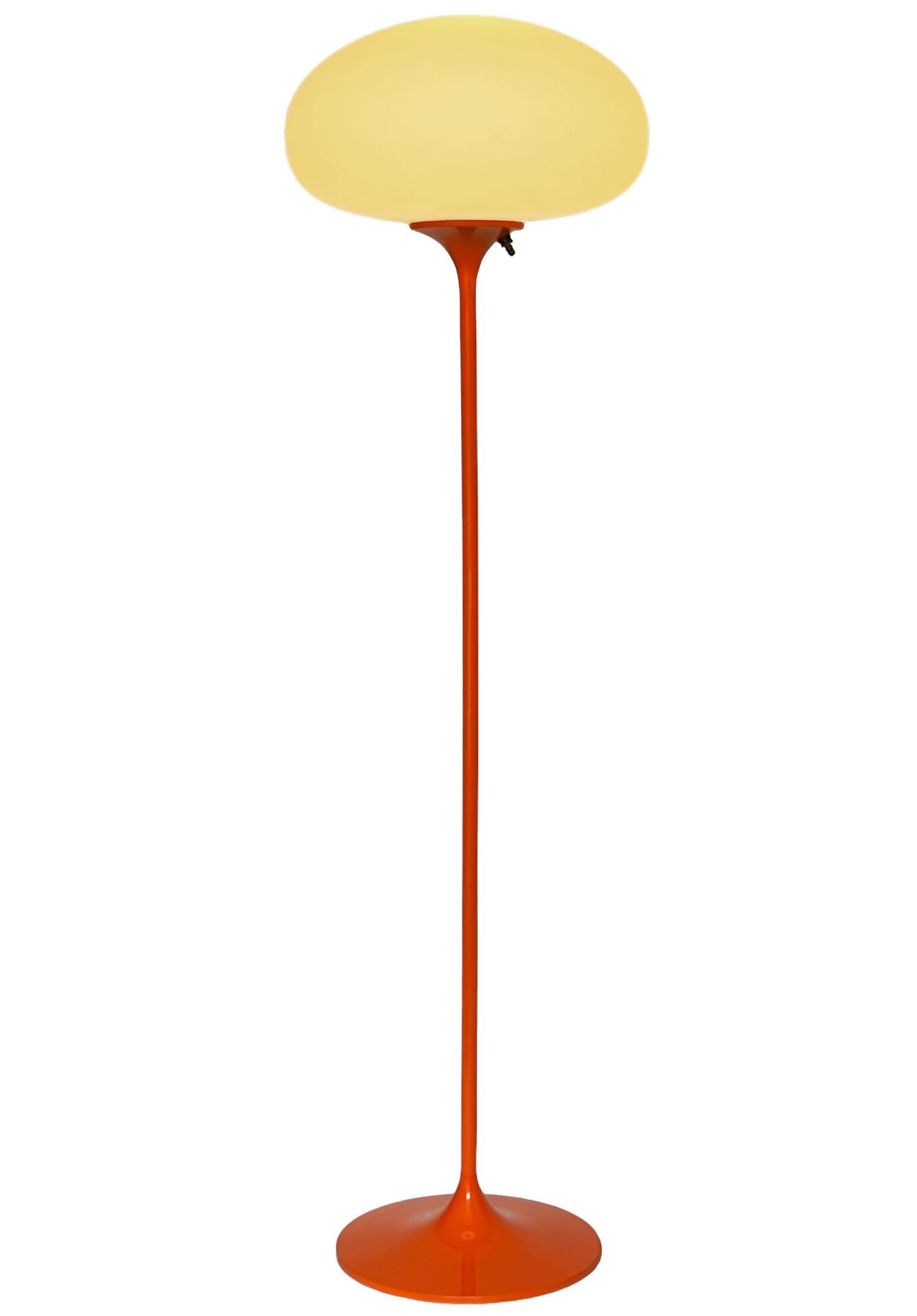 Un elegante pavimento a basso profilo realizzato da Design/One. Presenta una base principale in alluminio fuso a forma di tulipano scultoreo. La base della lampada è rifinita in un classico colore arancione retrò. La lampada in vetro smerigliato è