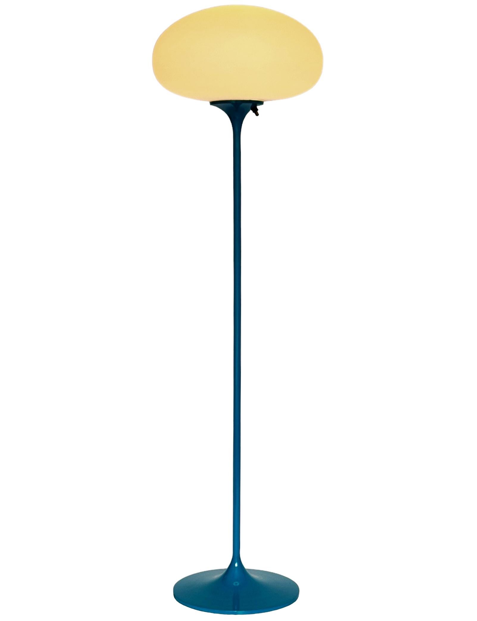 Ein schlanker, flacher Boden von Design-Line. Sie verfügt über einen Aluminiumguss-Sockel in einer skulpturalen Tulpenform. Der Sockel ist in einem klassischen Retro-Blau gehalten. Die Lampe aus mattiertem Glas ist mundgeblasen und gibt ein weiches,