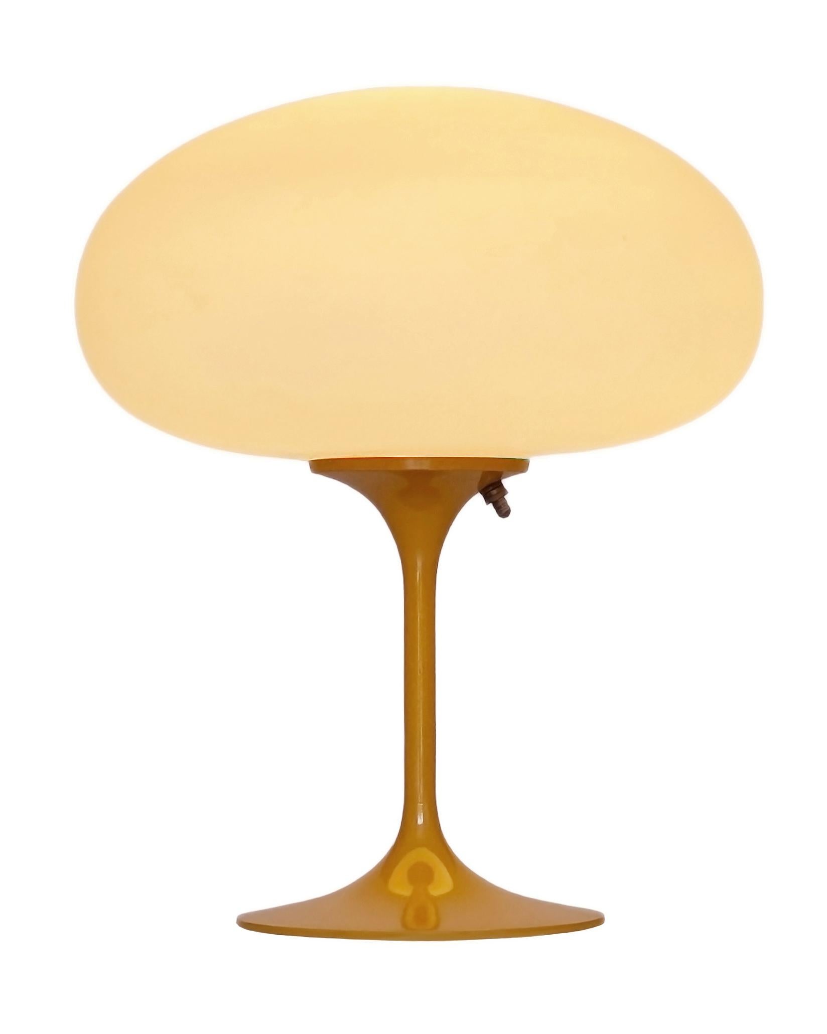 THIS ITEM IS ELIGIBLE FOR FREE SHIPPING!

A sleek stemlite table lamp made by Design Line. It features a cast aluminum main base in a sculptural tulip form. The lamp base is finished in a retro butterscotch color. The frosted glass lamp shade is