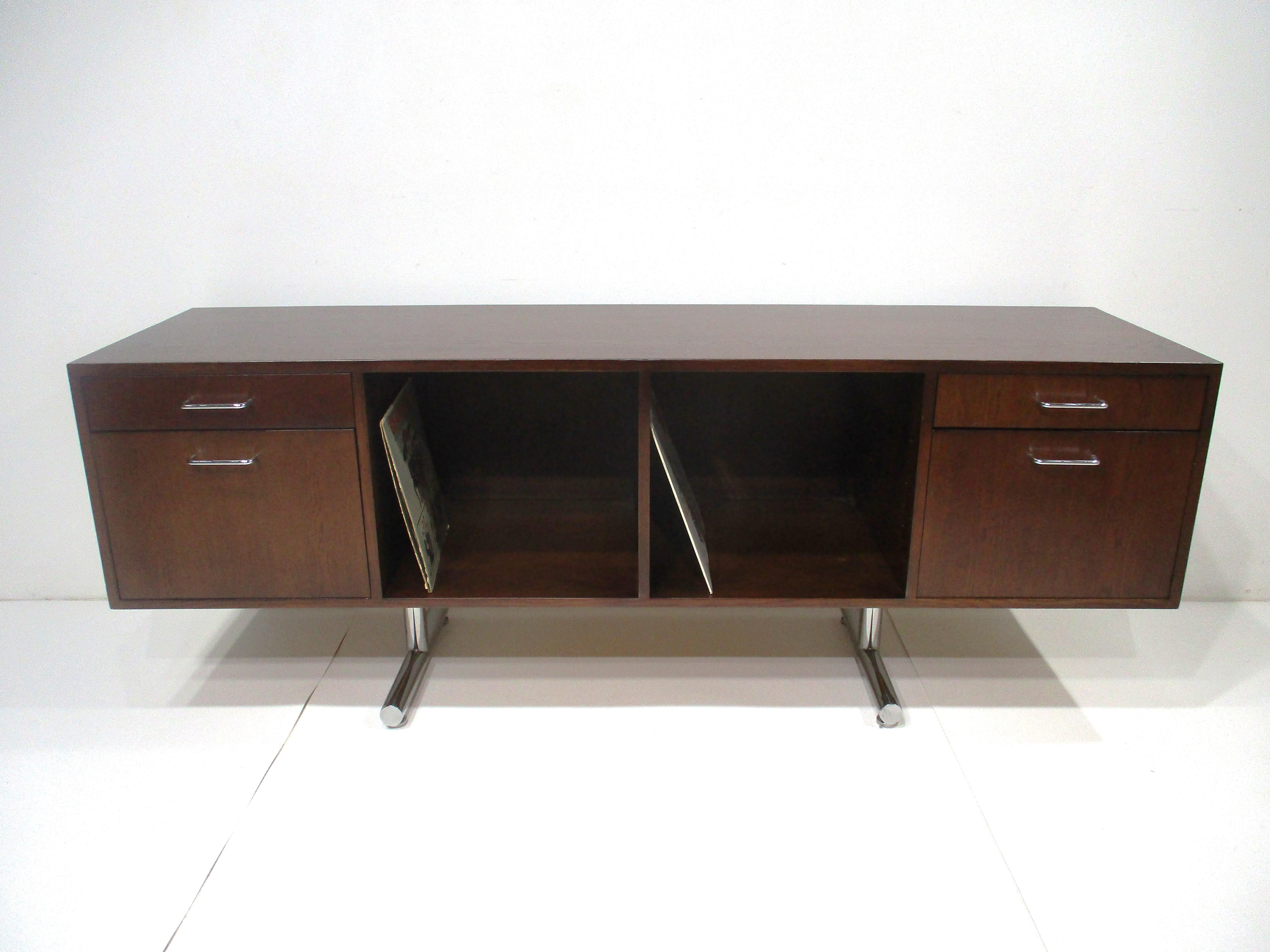 A very well crafted credenza or stereo entertainment cabinet in a dark walnut toned finish . Having two adjustable and removable shelves for records or your systems , two small drawers , two larger drawers to each side and chrome handles to the