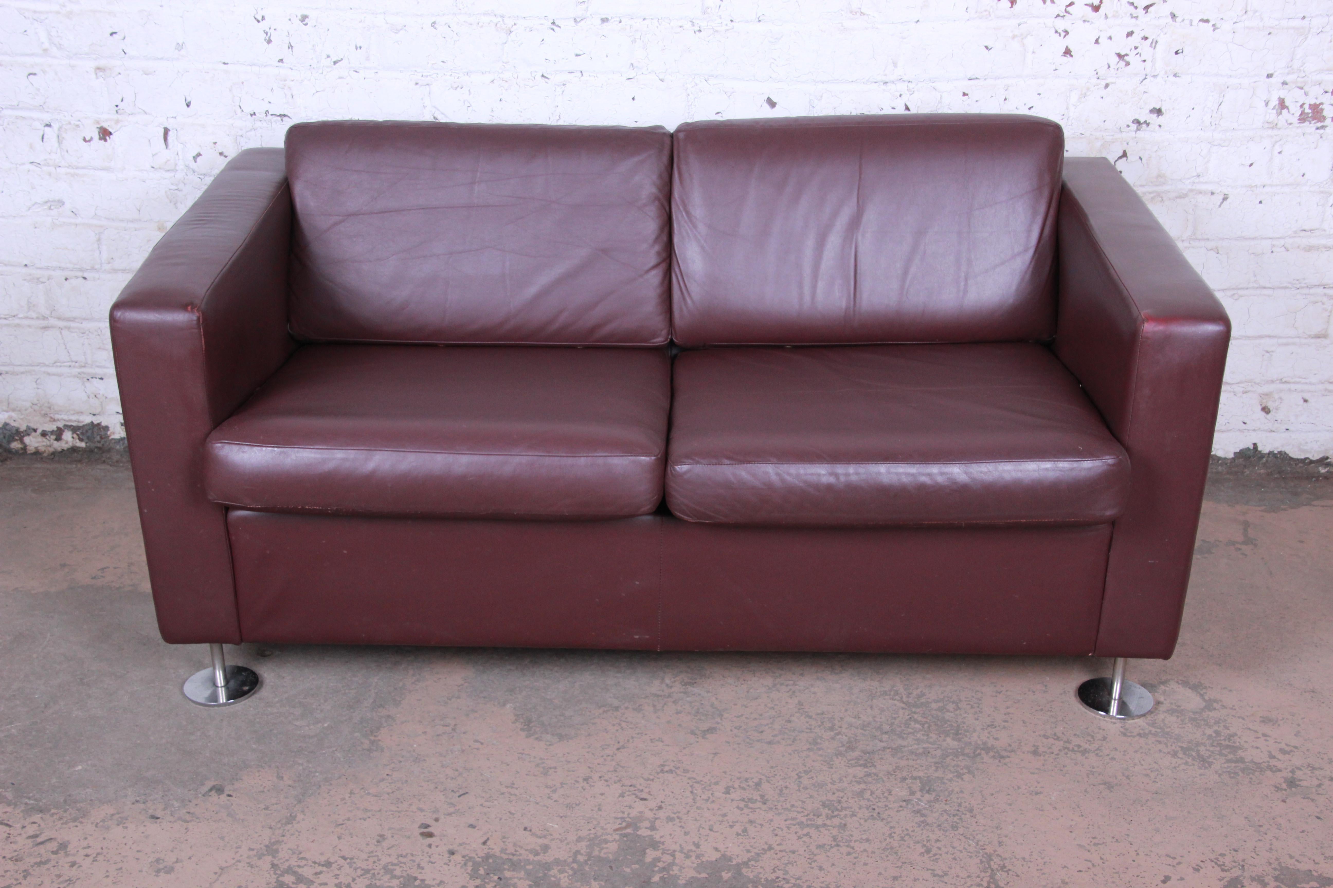 A gorgeous leather tuxedo loveseat by Stendig. The sofa features high grade burgundy leather and chrome feet. The leather has some patina and is nicely worn in from age and use. The seats are still nice and firm. Made in Switzerland by Stendig and