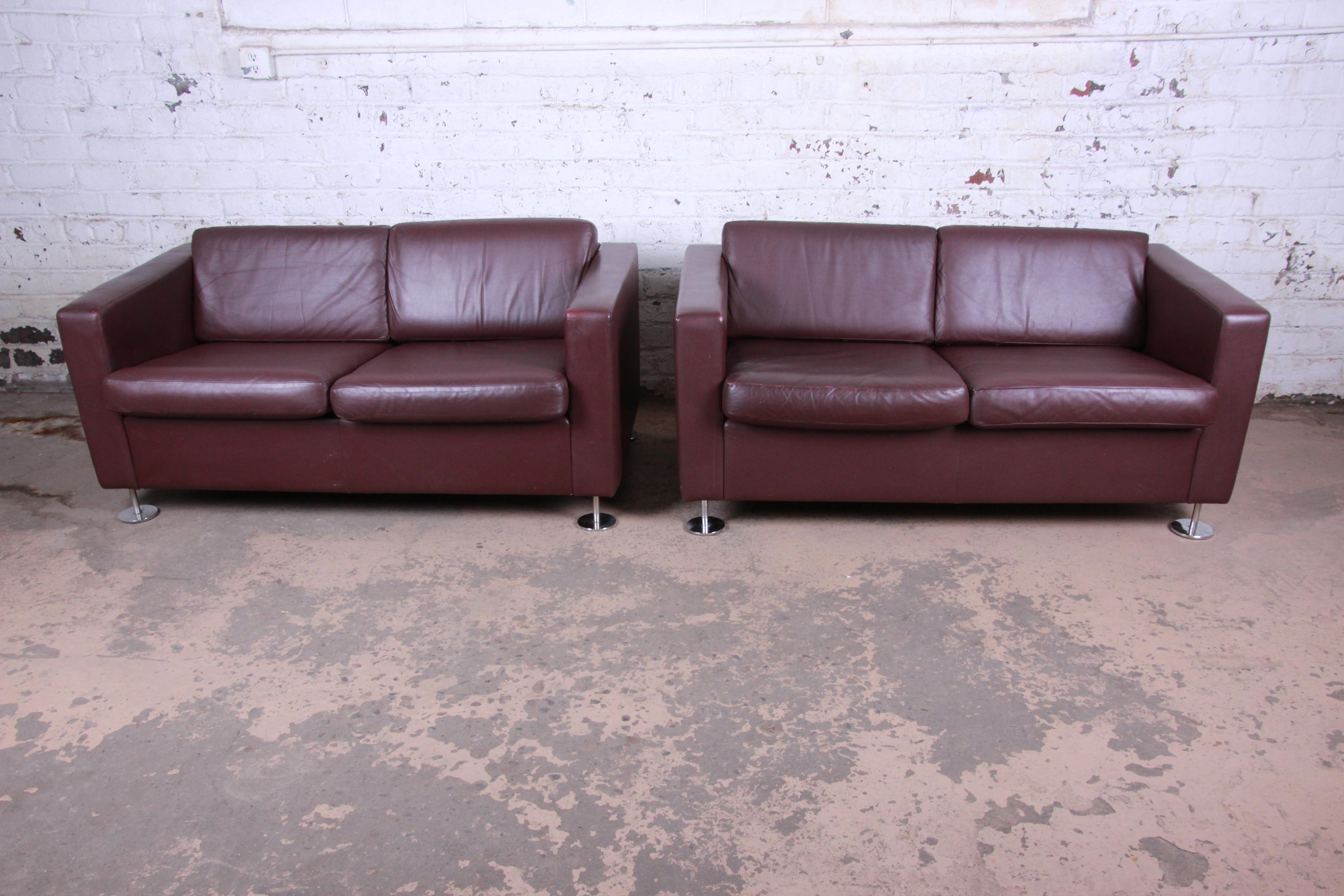 A gorgeous pair of leather tuxedo love seats by Stendig. The sofas feature high grade burgundy leather and chrome feet. The leather has some patina and is nicely worn in from age and use. The seats are still nice and firm. Made in Switzerland by