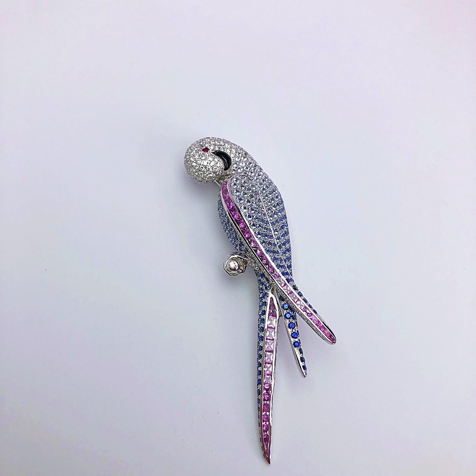 Designed in 18 karat white gold, this very graceful parrot brooch is a work of art. Pave white diamonds are set and subtly change to shades of blue and pink sapphires. A single round ruby is set for the eye and black onyx for the beak. The parrot